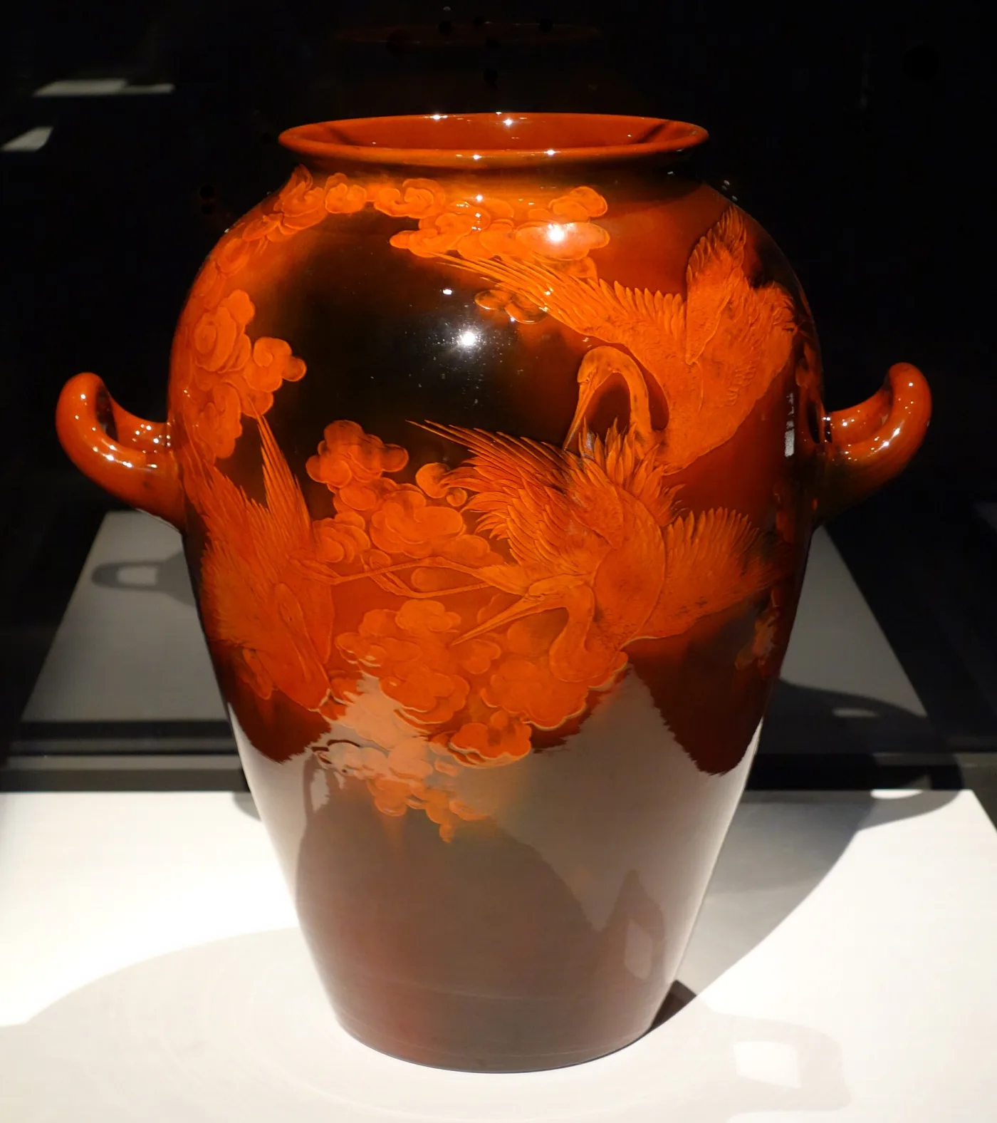 Bulbous two-handled vase in glossy dark brown shading to bright orange, slip-painted with large orange and yellow blossoms and dark leaves