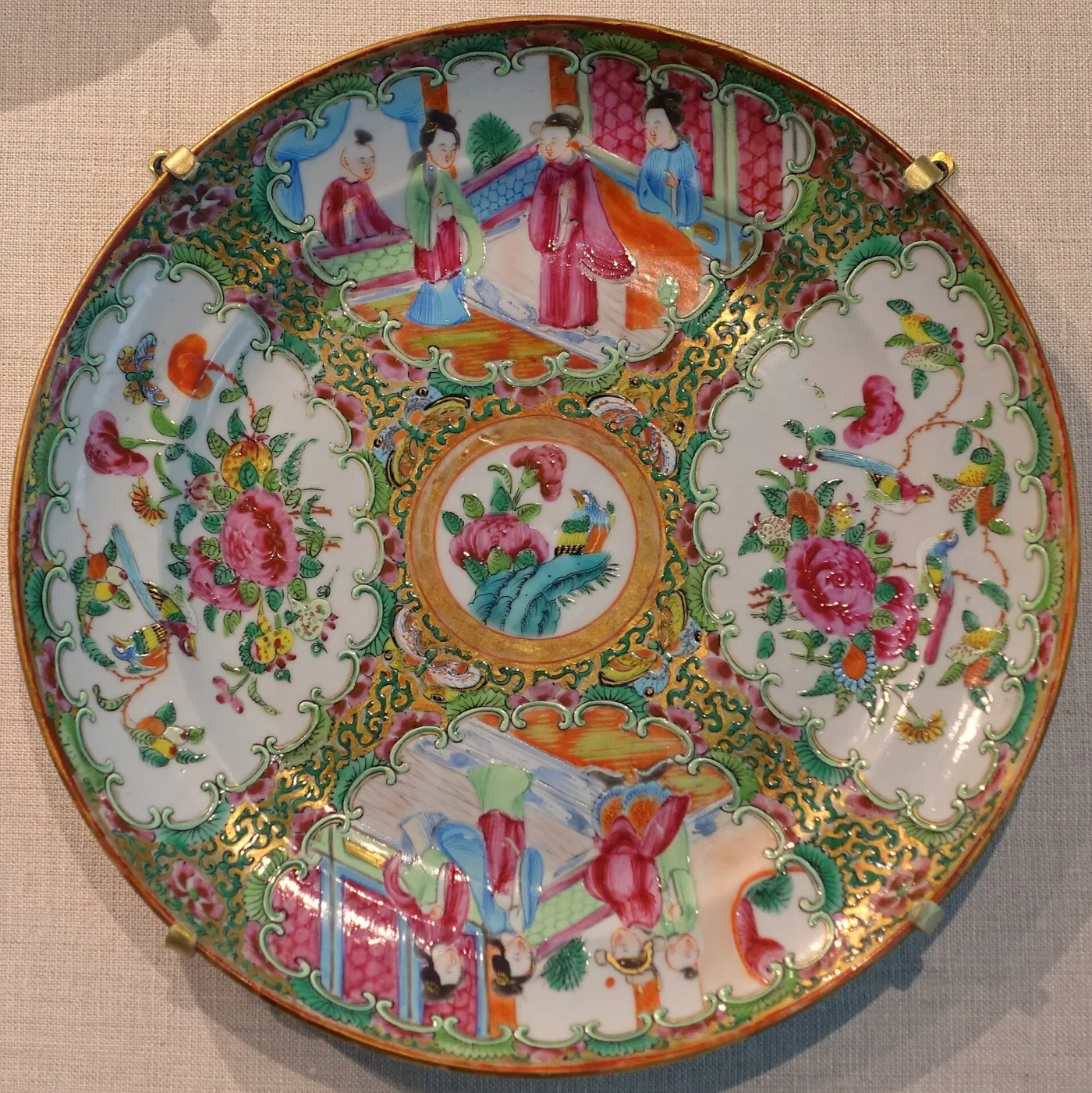 Chinese rose medallion plate of 1840 to 1900 with four rim panels alternating between groups of figures and birds with peonies, around a gilt-ringed central roundel holding a bird on a rock among peonies, on a dense green and gilt filler ground