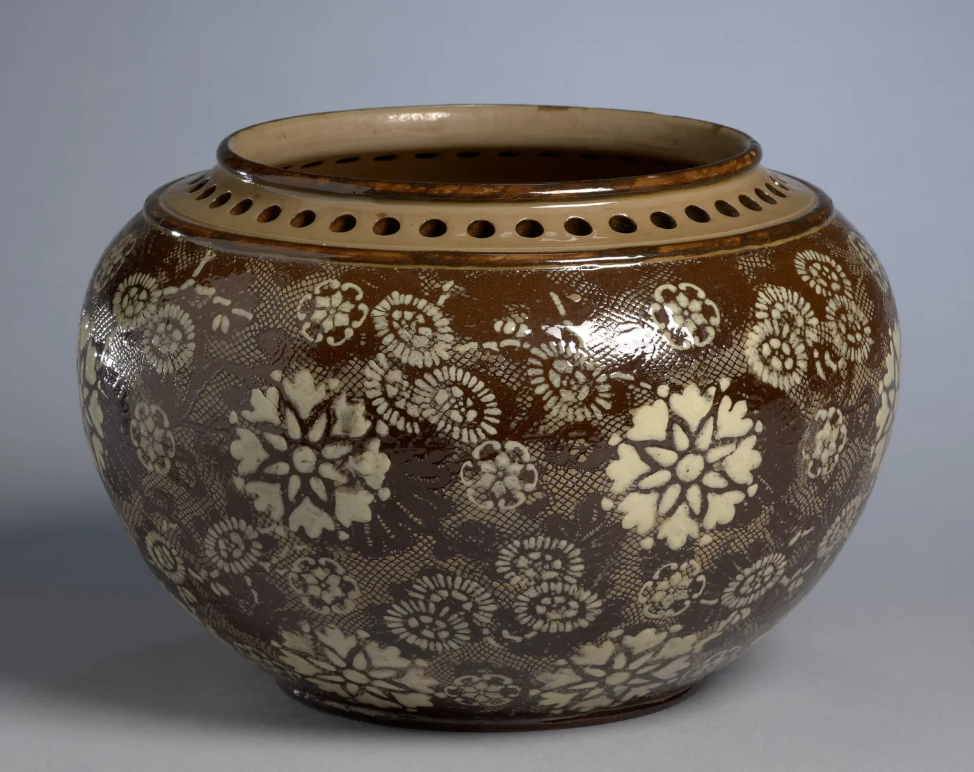 Wide low stoneware bowl in warm brown, its body covered with regularly spaced applied white flower rosettes above a band of small beads, with a pierced rim