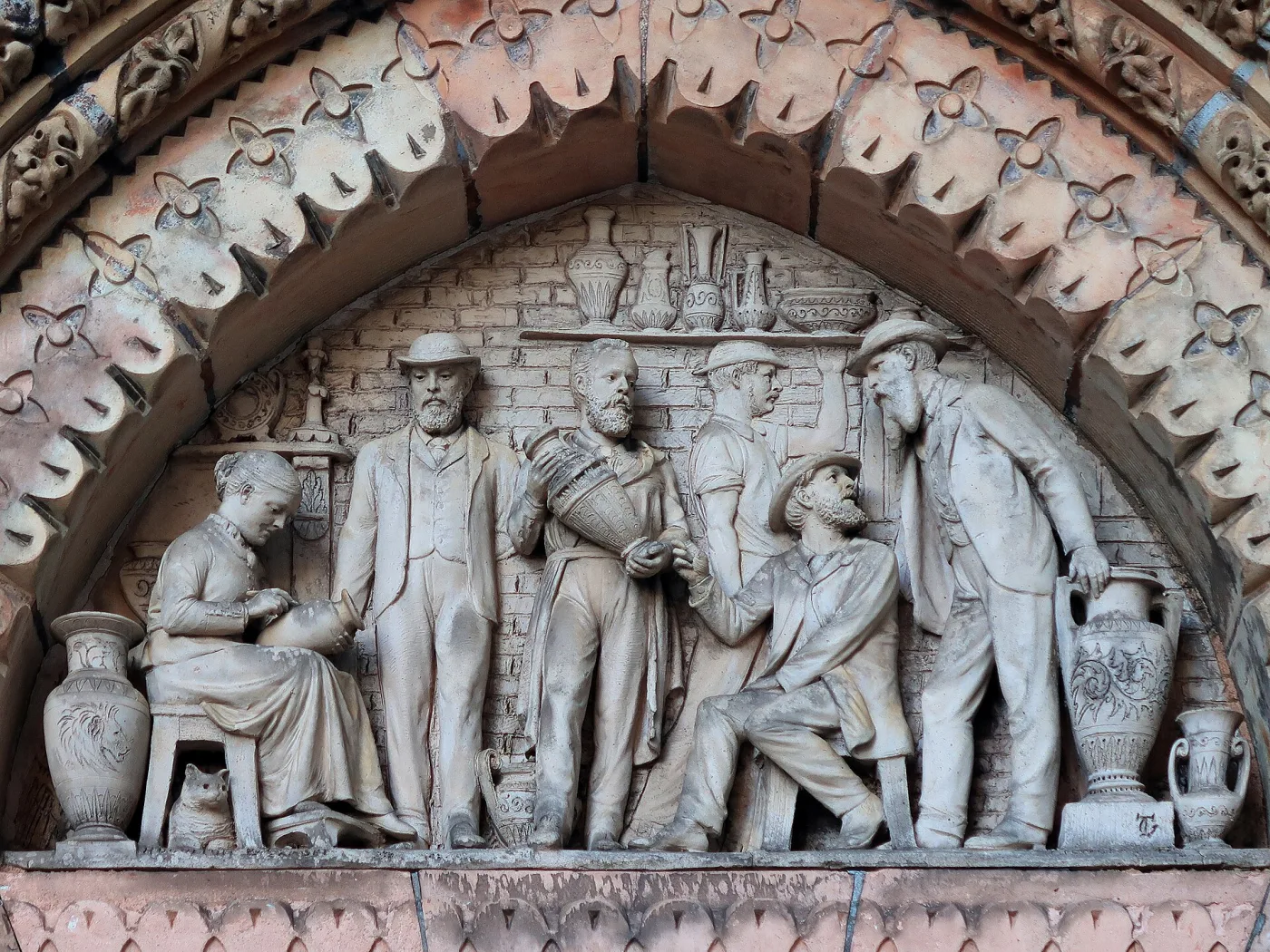 Semicircular architectural relief in pale terracotta set above a doorway, modelled with figures at work in a pottery: a man throwing at a wheel, others carrying and decorating large vases