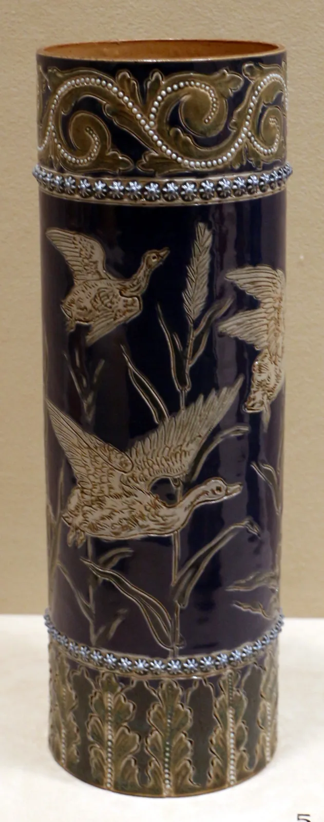 Tall cylindrical stoneware vase in deep cobalt blue, decorated in relief with pale birds among trailing foliage, with a band of moulded ornament at the shoulder and a stiff leaf border at the foot