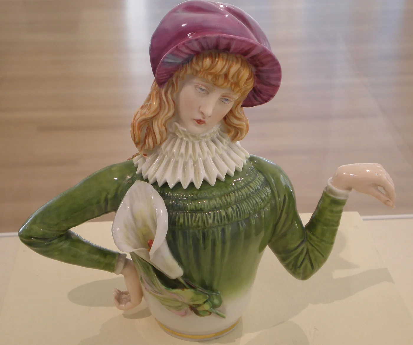 Teapot modelled as a young woman in a green dress and a pink hat, her bent arms forming the spout and handle, holding a white lily