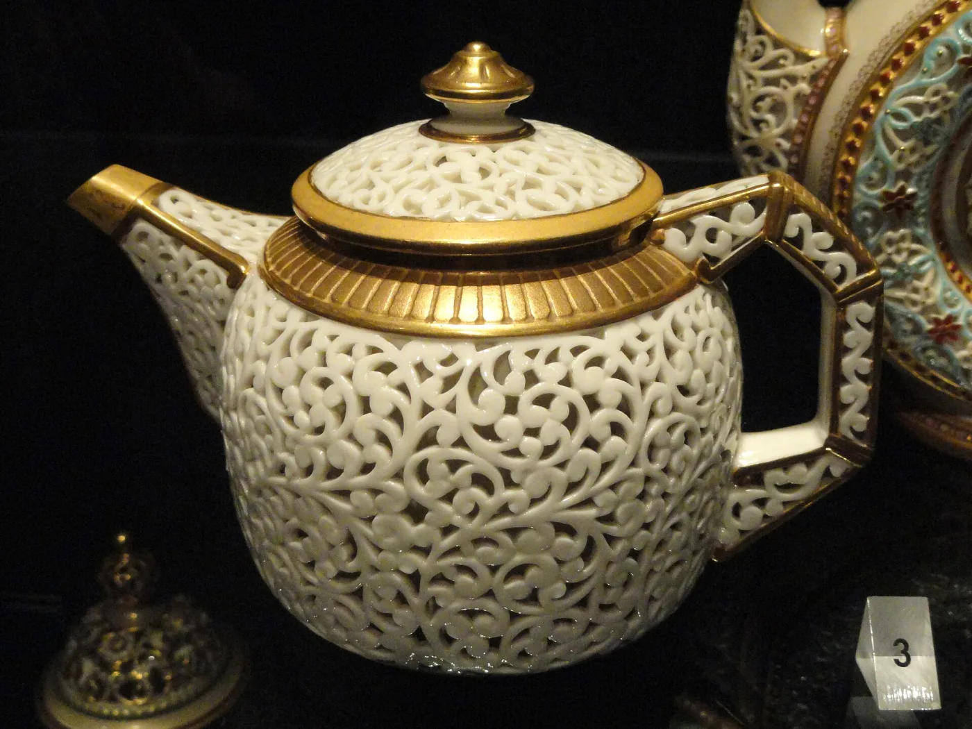 Small globular teapot pierced all over with a dense scrolling openwork pattern, with heavy gilding on the rim, spout, handle and finial