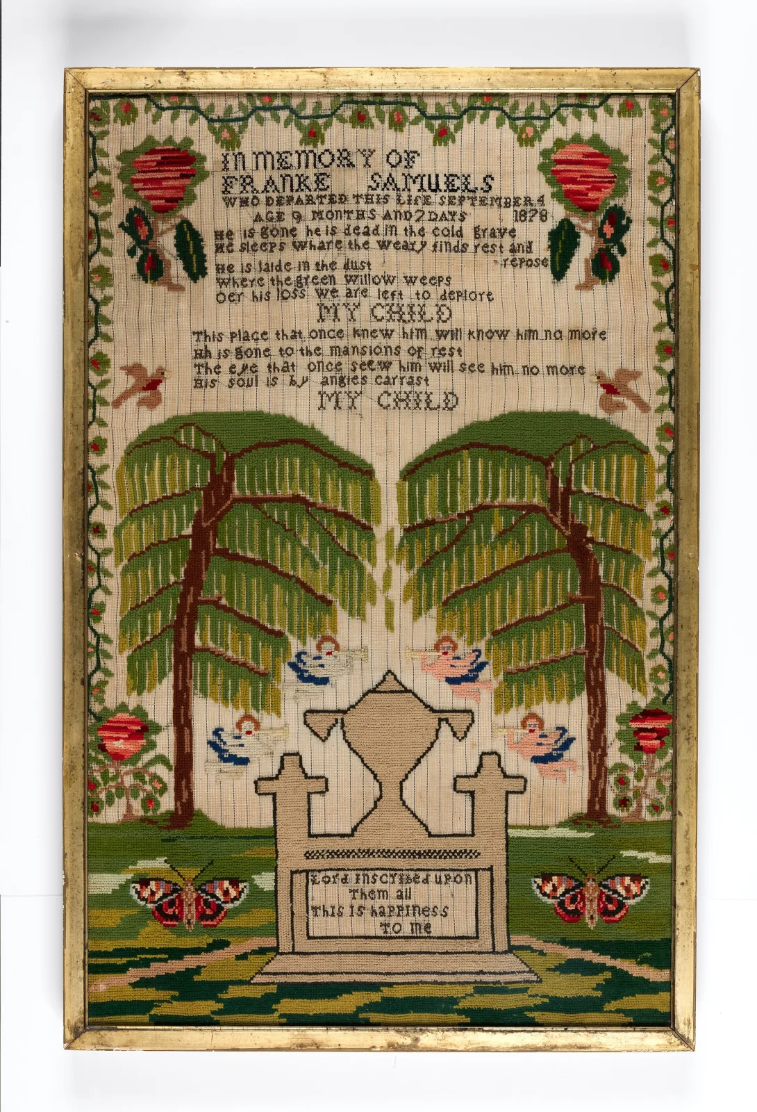 Framed memorial sampler worked in coloured wool, with a stitched inscription at the top, two large weeping willows, an urn on a tomb, four flying cherubs and butterflies