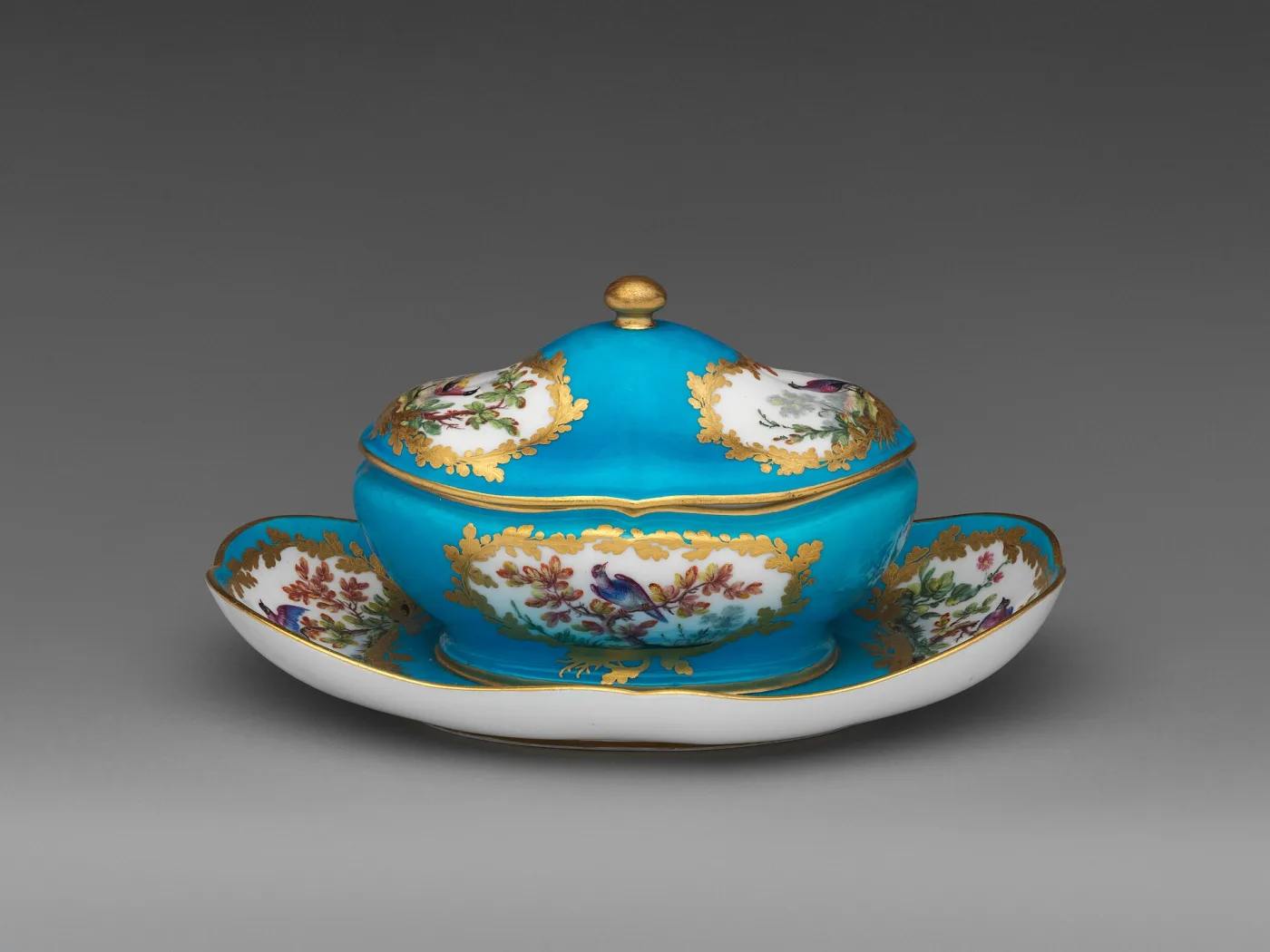 Turquoise-blue Sèvres sugar bowl and cover on a matching oval stand, with gilt oak-leaf cartouches framing painted birds