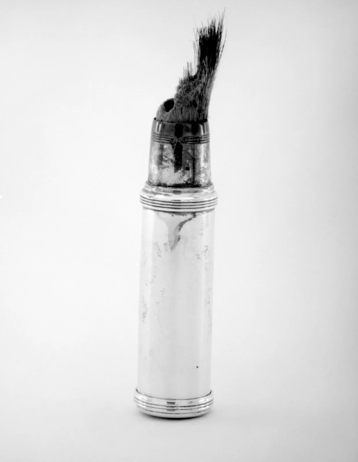 Shaving brush with a dark bristle head set into a plain cylindrical silver handle, standing upright against a white ground