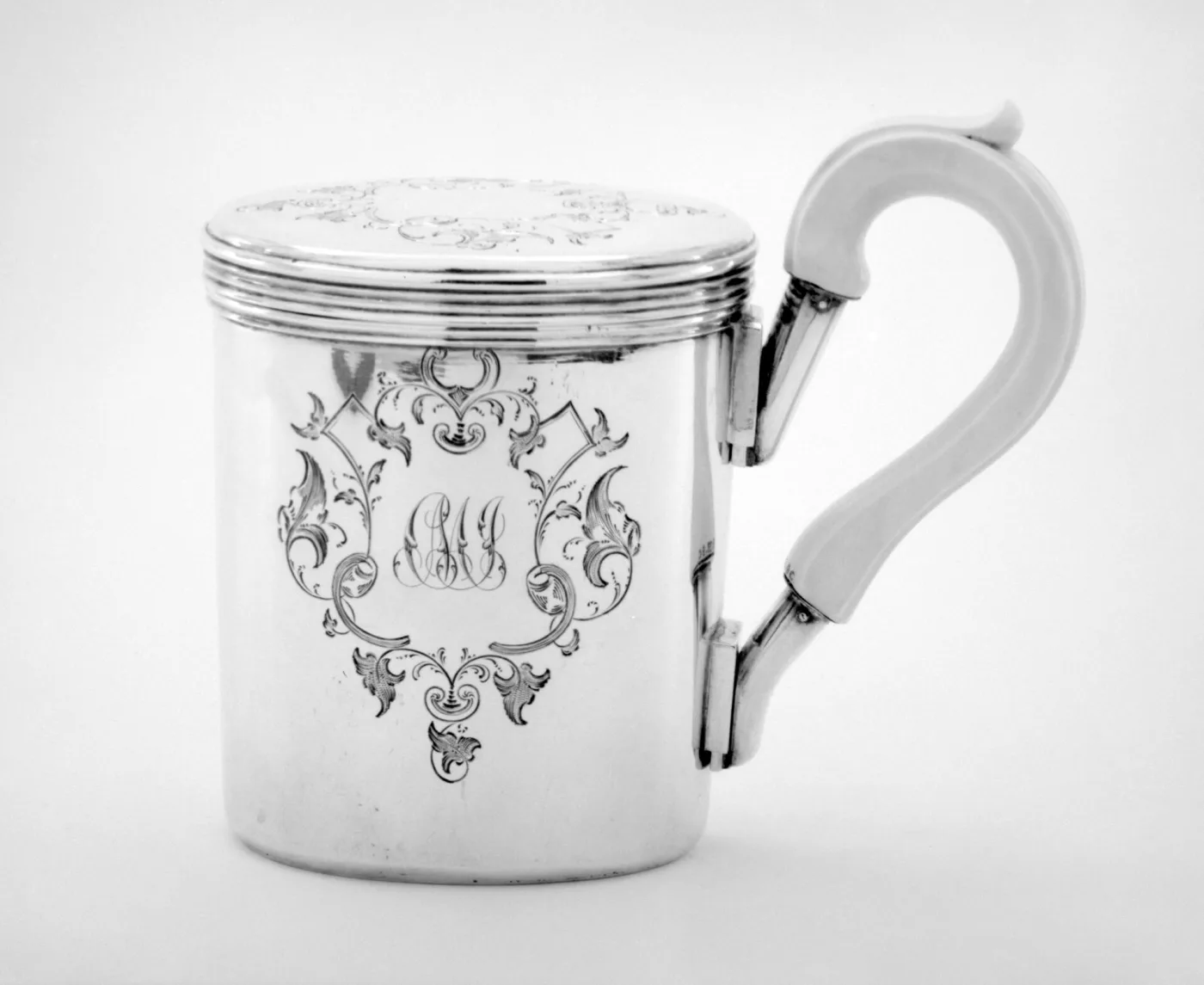 Silver shaving cup with a domed cover and a hinged handle standing beside a matching shallow silver soap dish, both engraved with foliate cartouches
