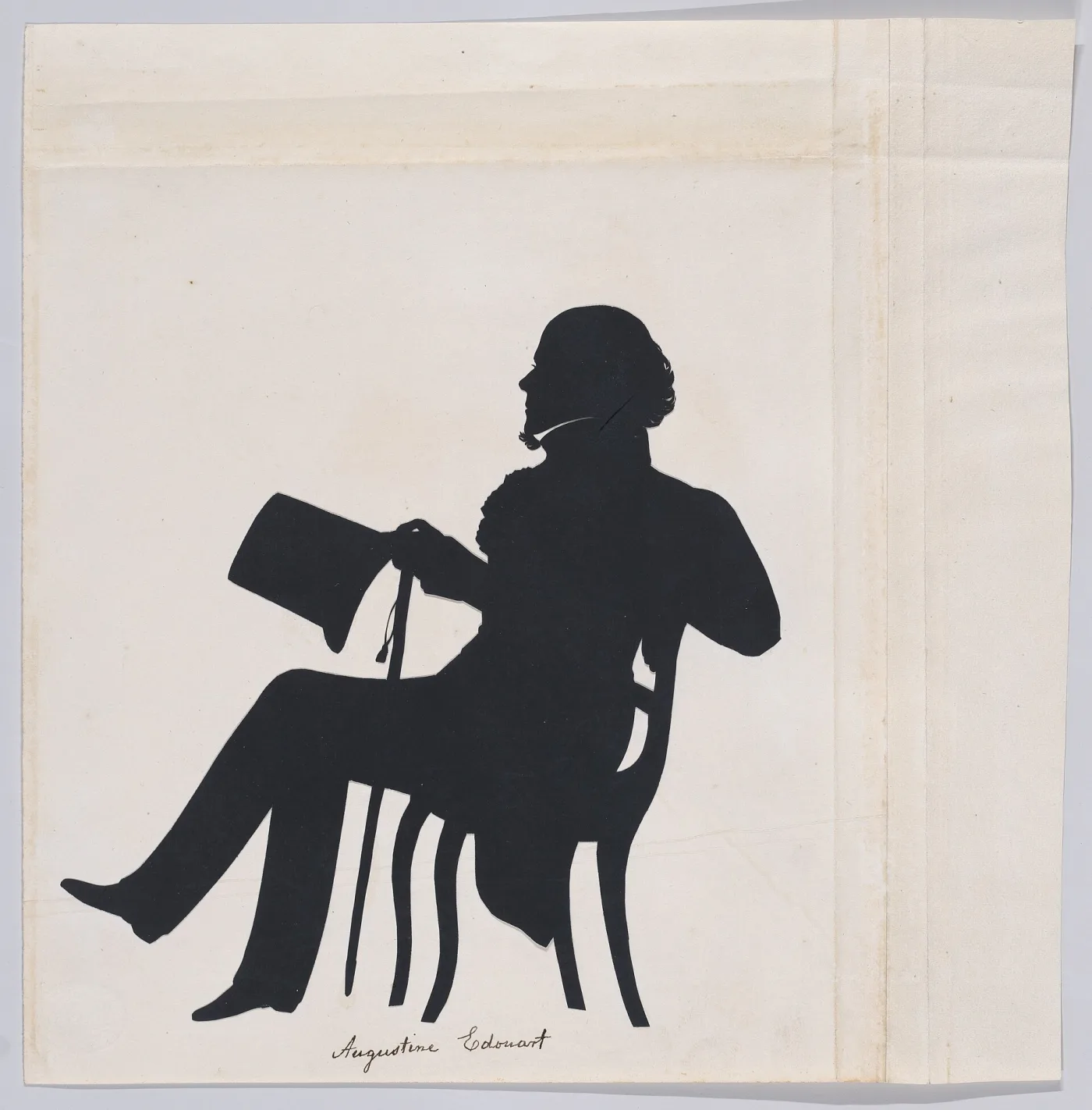 Silhouette of a seated man reading, cut in black and pasted on a large plain sheet whose folds and edges are visible, with a signature in ink beneath the figure