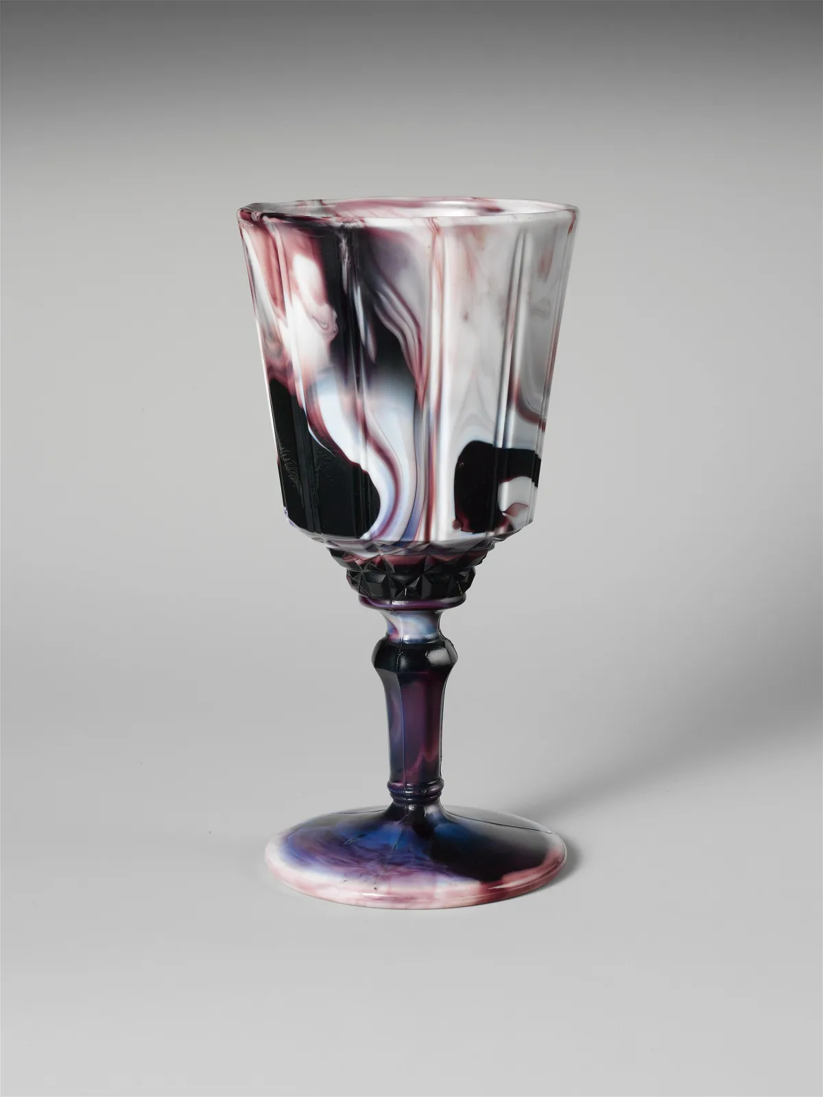 Purple and white marbled glass goblet on a knopped stem and spreading foot, the bowl panelled with a band of pressed diamond points beneath it