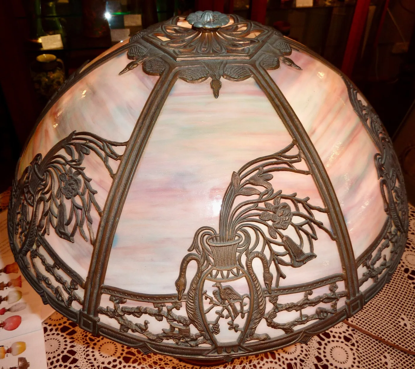 Domed lamp shade of six curved panels of pink, green and caramel streaked glass held behind an openwork cast metal overlay of swans, urns, flowers and birds with a green patina
