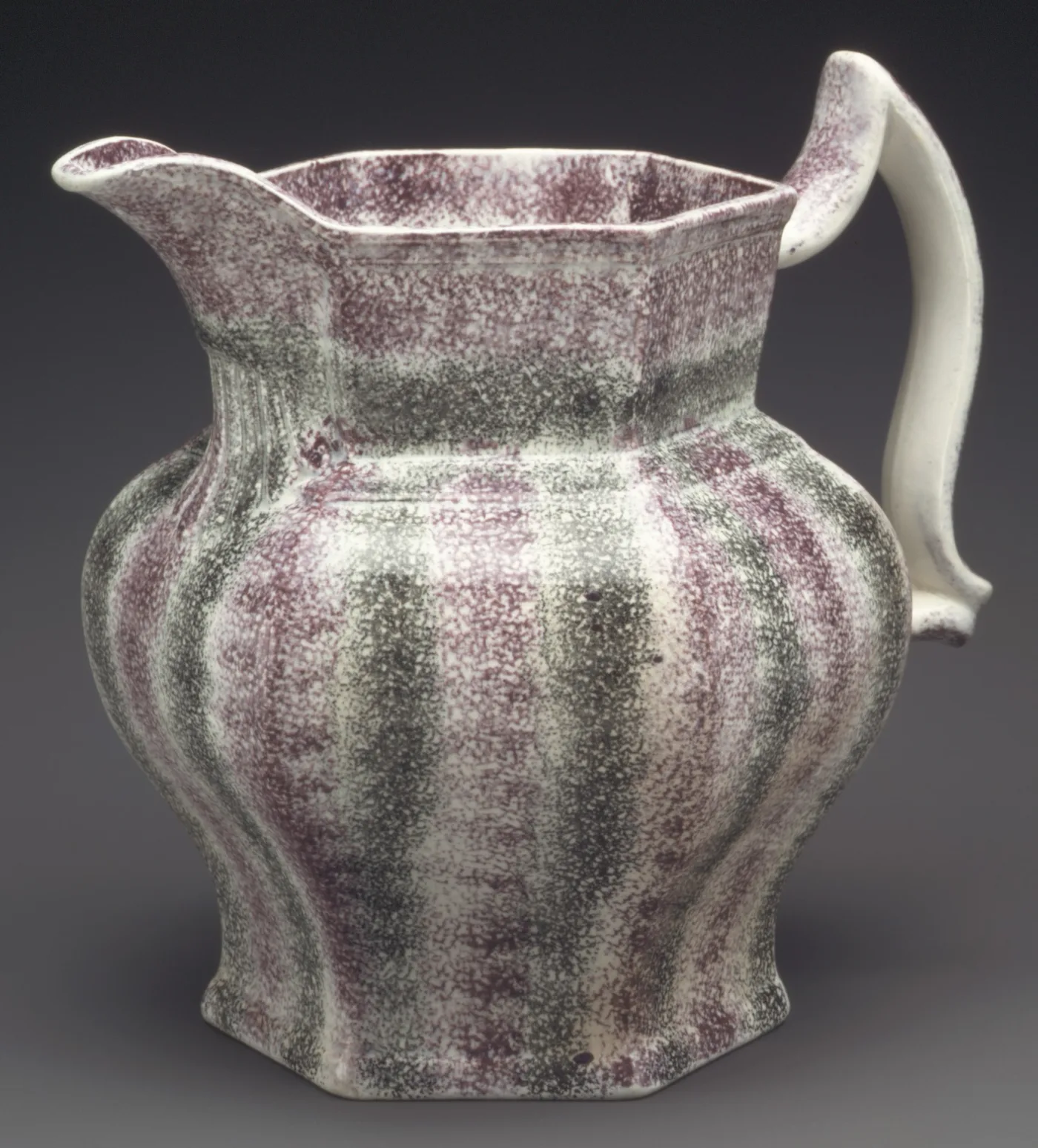 A large octagonal jug covered all over in purple and black sponging that follows the vertical facets of its body, with a plain white handle
