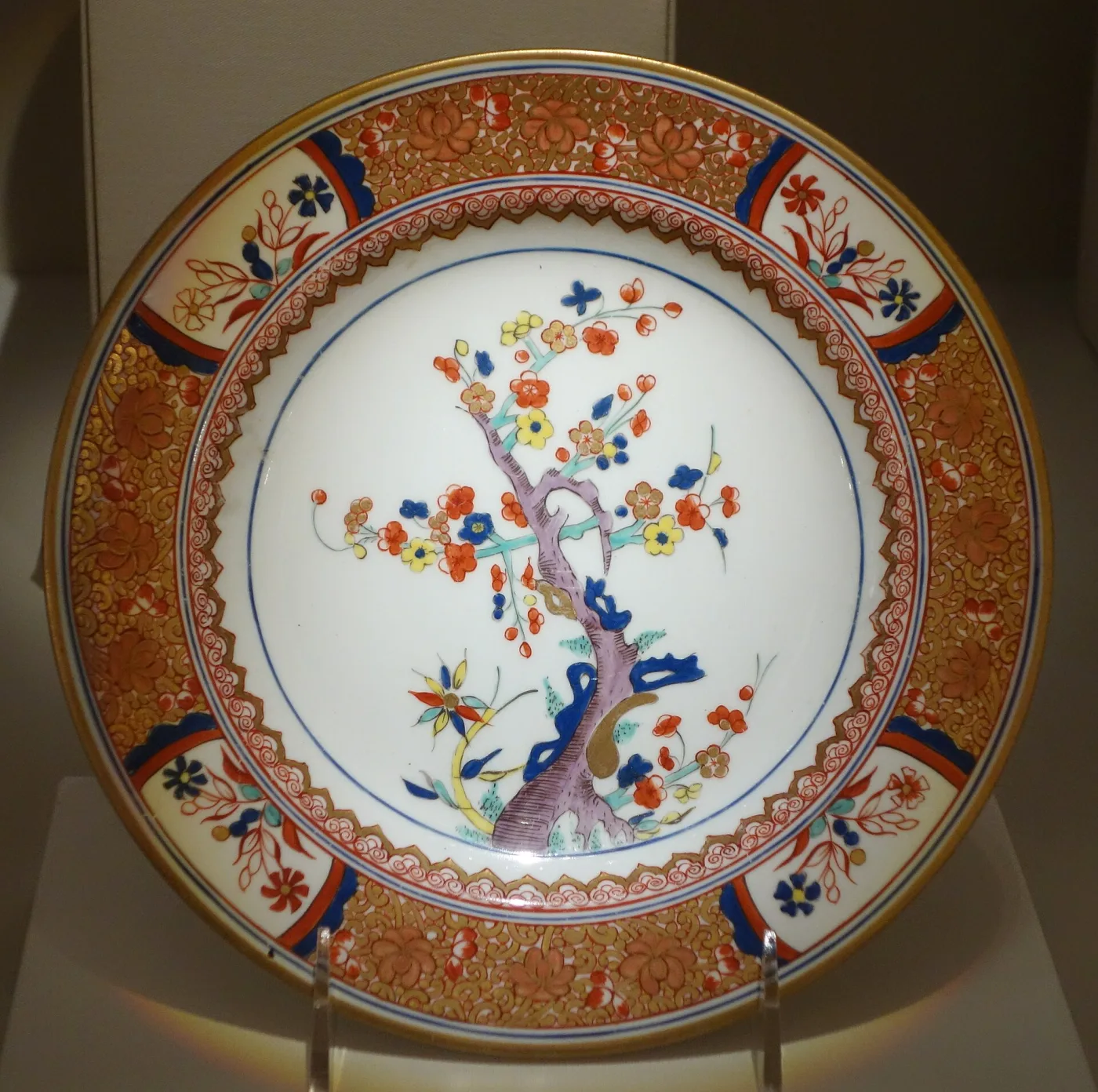 Spode porcelain plate of about 1792 to 1794, its centre painted with a flowering tree growing from blue rockwork in orange, blue and yellow, inside a broad orange and gilt border broken by dark blue panels