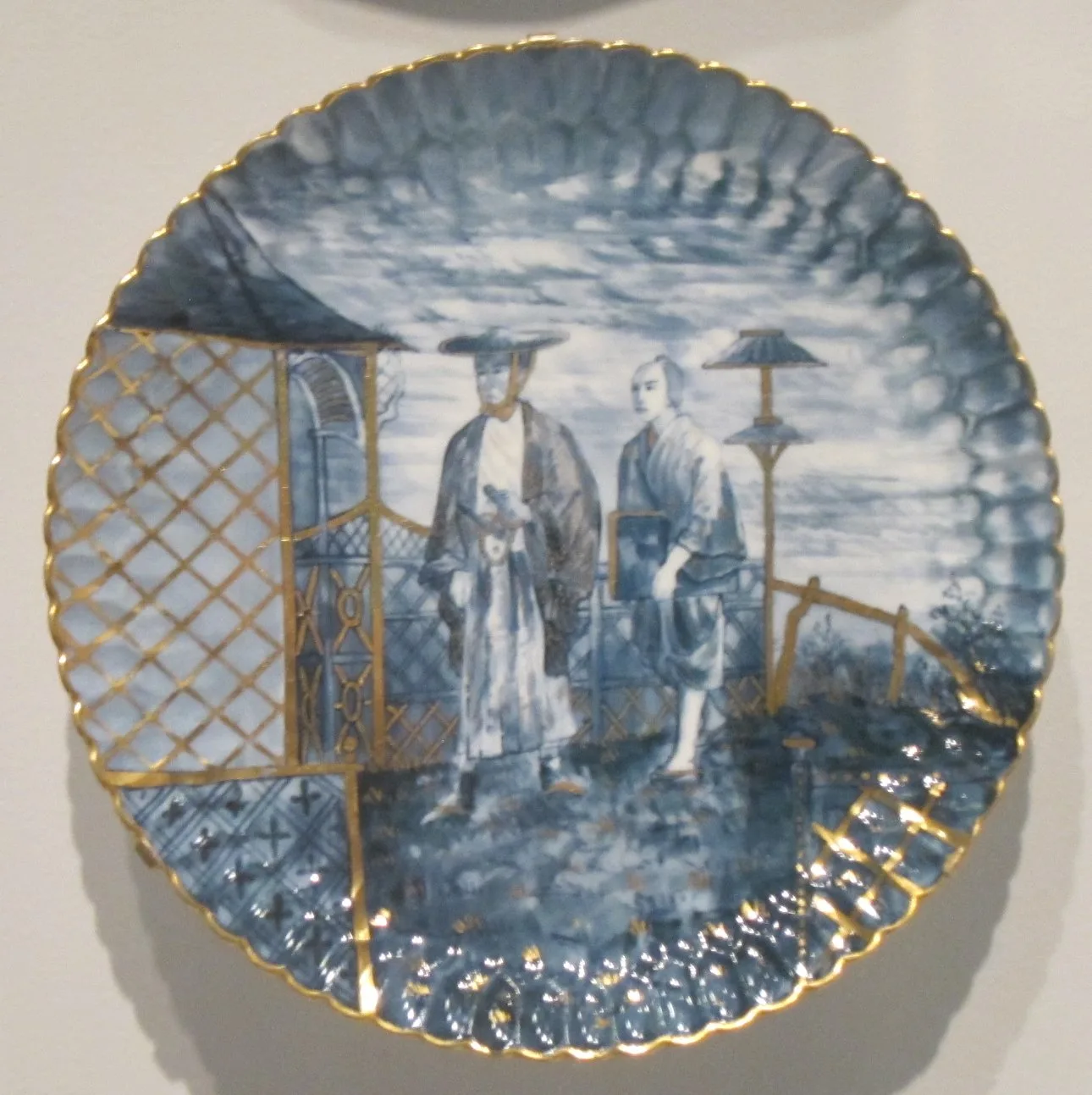 Late nineteenth-century plate printed in soft blue with two figures in Japanese dress standing under a parasol beside a trellis, within a wide moulded gadrooned border and gilt rim