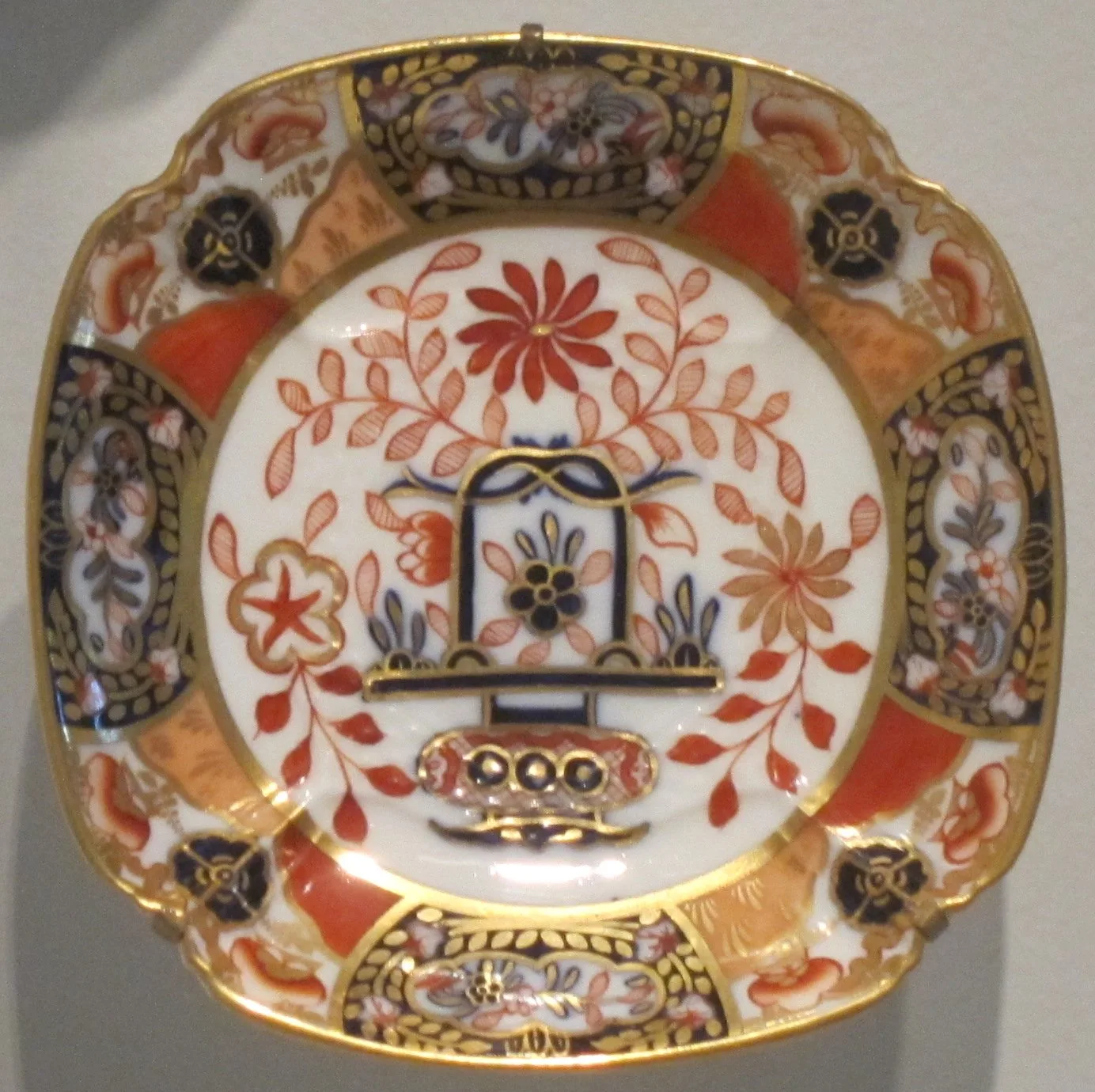 Square dish with rounded corners in the Imari palette, cobalt and gilt panels at the corners, orange grounds between them and a central flower spray in a white well