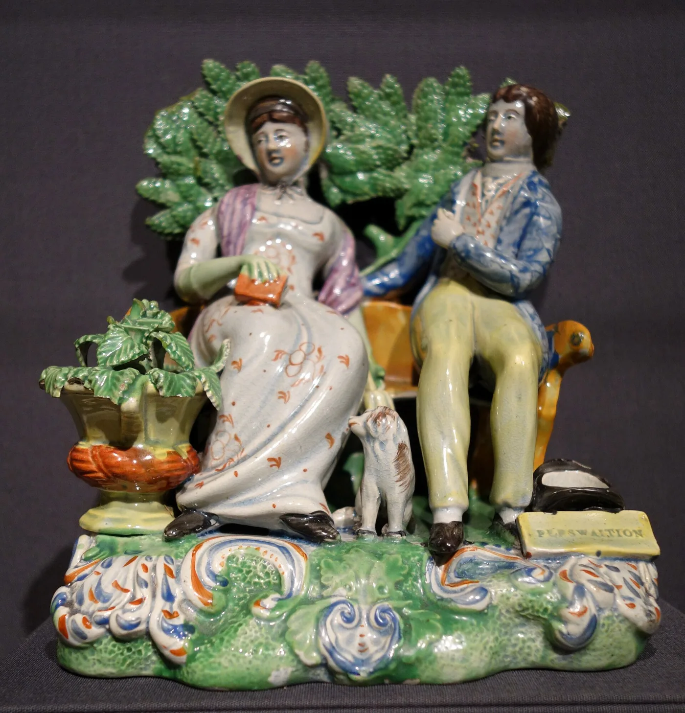 Pottery group of a seated woman with a book and a young man on a bench, a leafy bocage behind and a plaque on the base lettered PERSWAITION