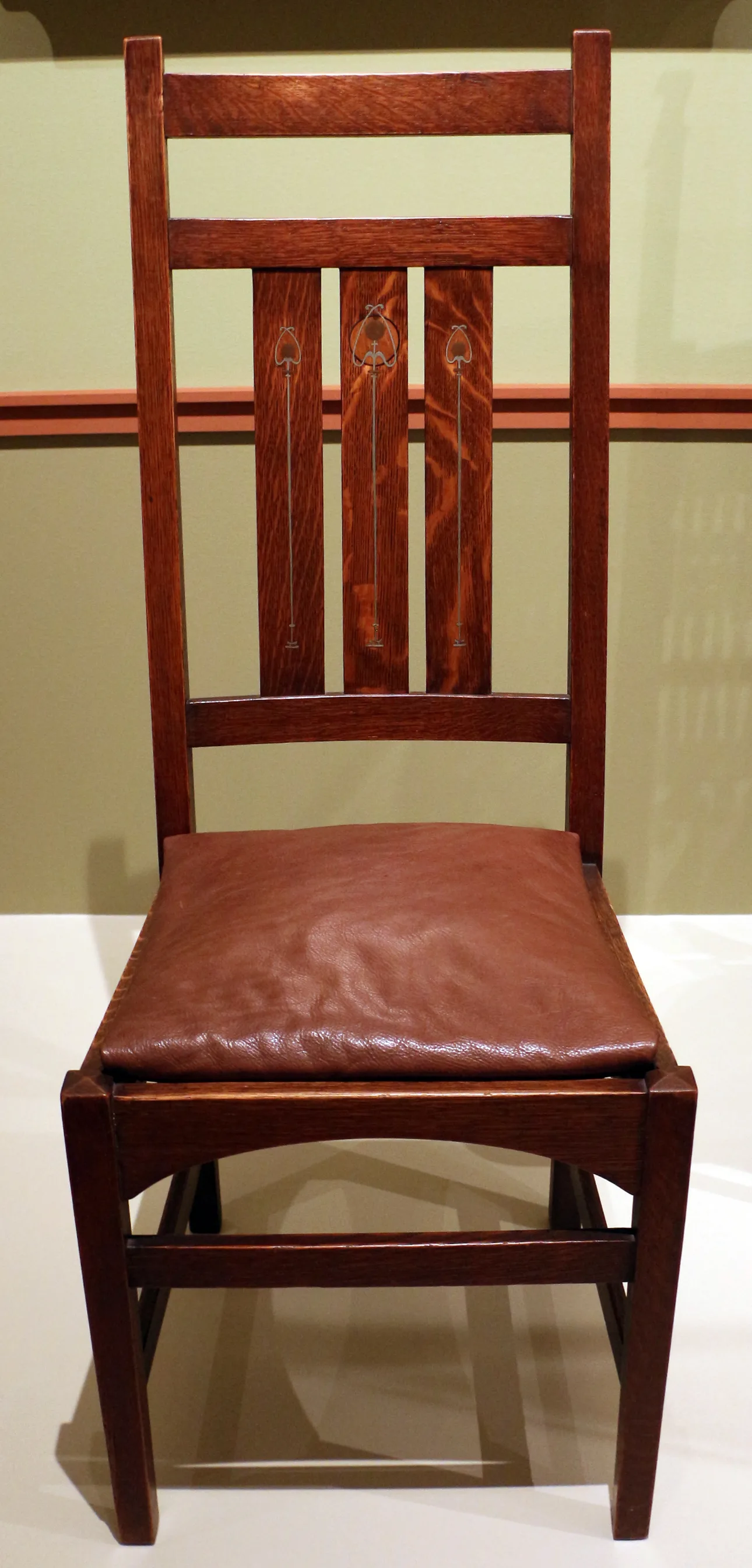 Tall-backed oak side chair with three vertical splats inlaid with thin metal lines ending in stylised buds, a brown leather seat and an arched front rail