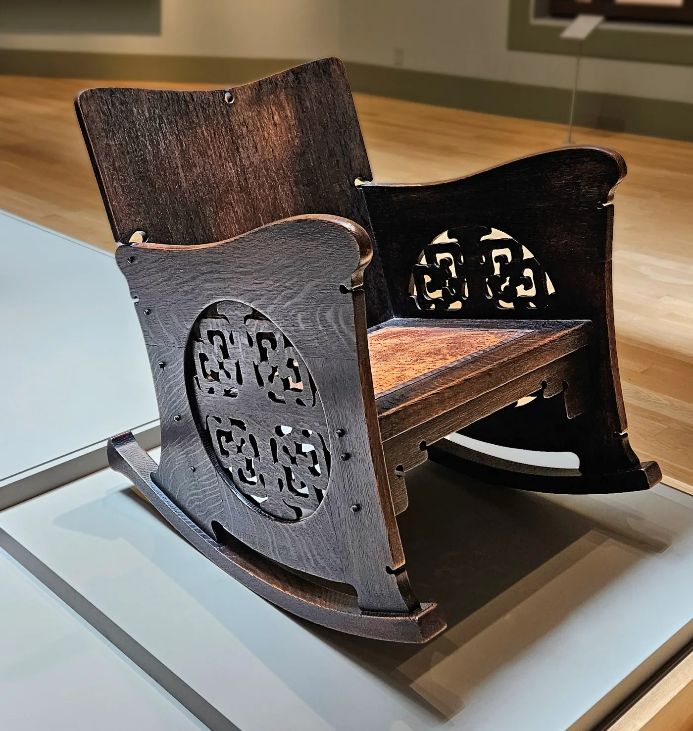 Dark oak rocking chair with curved side panels pierced by circular fretwork and a plain shaped back board