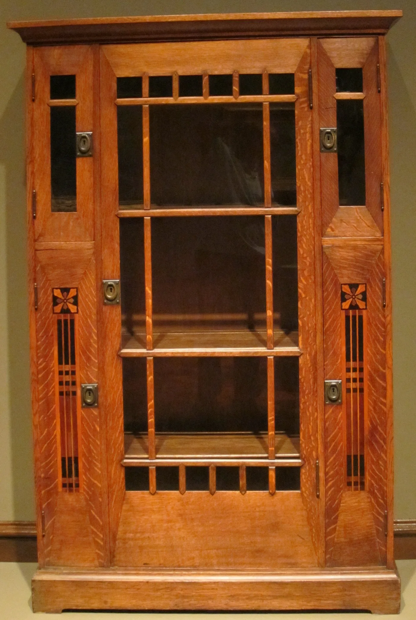 Light-finished oak china cabinet with a mullioned glass door, side doors inlaid with dark and pale flower panels, and vivid ray fleck across the frame