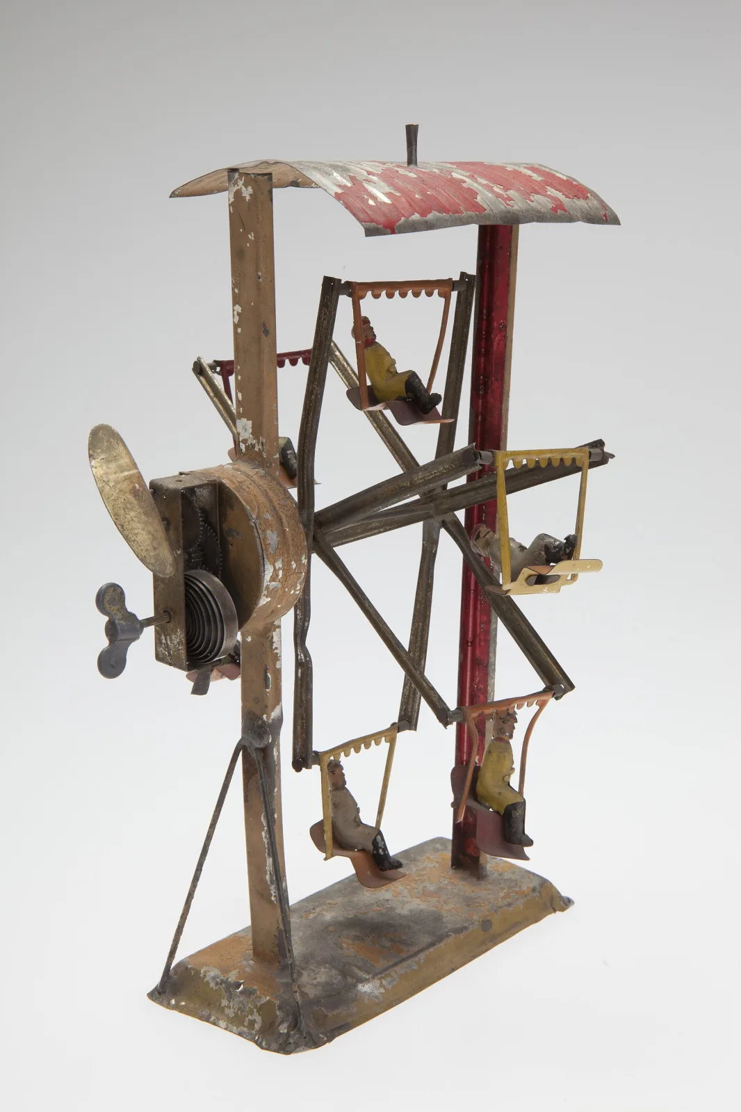 Clockwork tin toy Ferris wheel of about 1900, an open framework of painted strips carrying six swinging cars, with a striped canopy at the top and a winding mechanism at the base