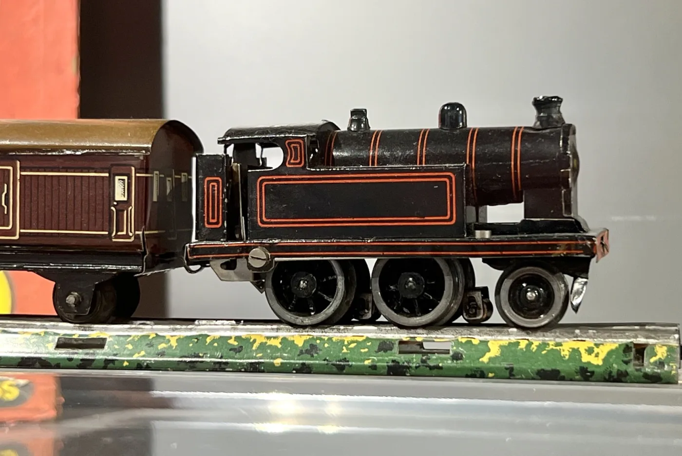 Small black tinplate tank locomotive standing on track printed with green grass and ballast