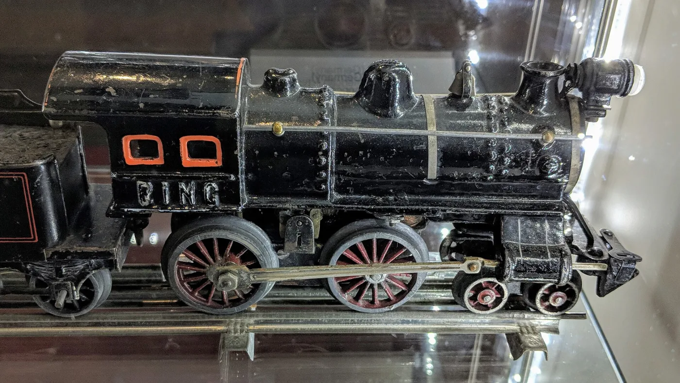 Black tinplate locomotive with a cowcatcher and red-spoked wheels, the name BING raised on the cab side