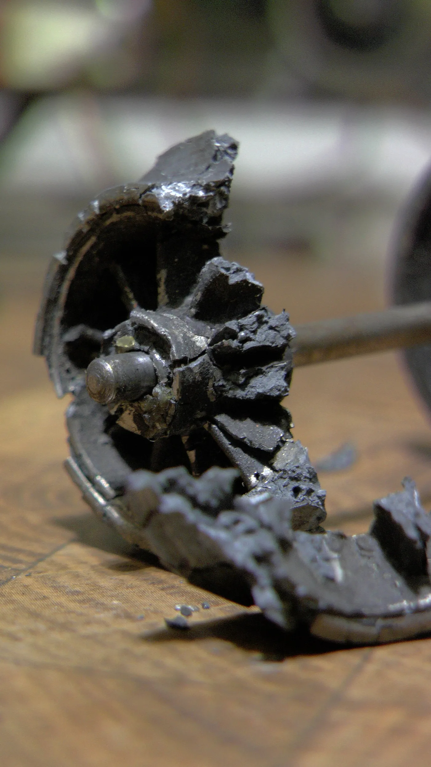 Die-cast toy train wheel broken into loose fragments on its axle, with crumbs of metal fallen beside it
