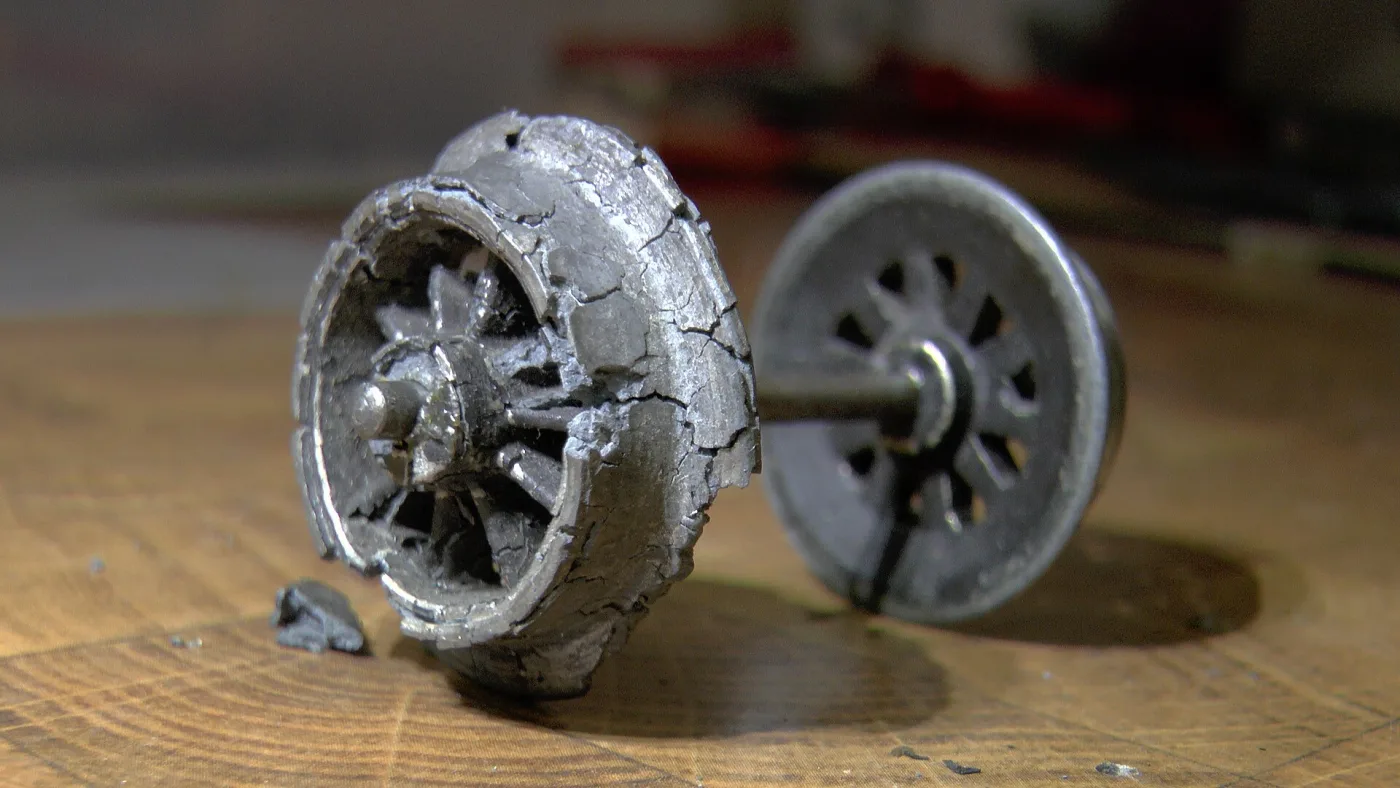Toy locomotive wheelset with one die-cast wheel swollen and cracked apart while the other stays sound