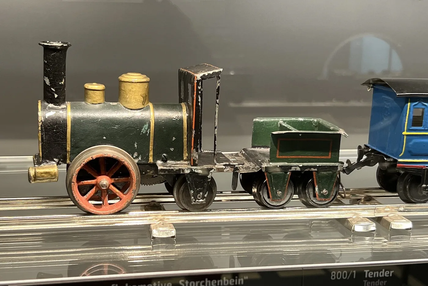 Small dark green tinplate locomotive with tall funnel, brass domes, one large red spoked wheel and a low tender