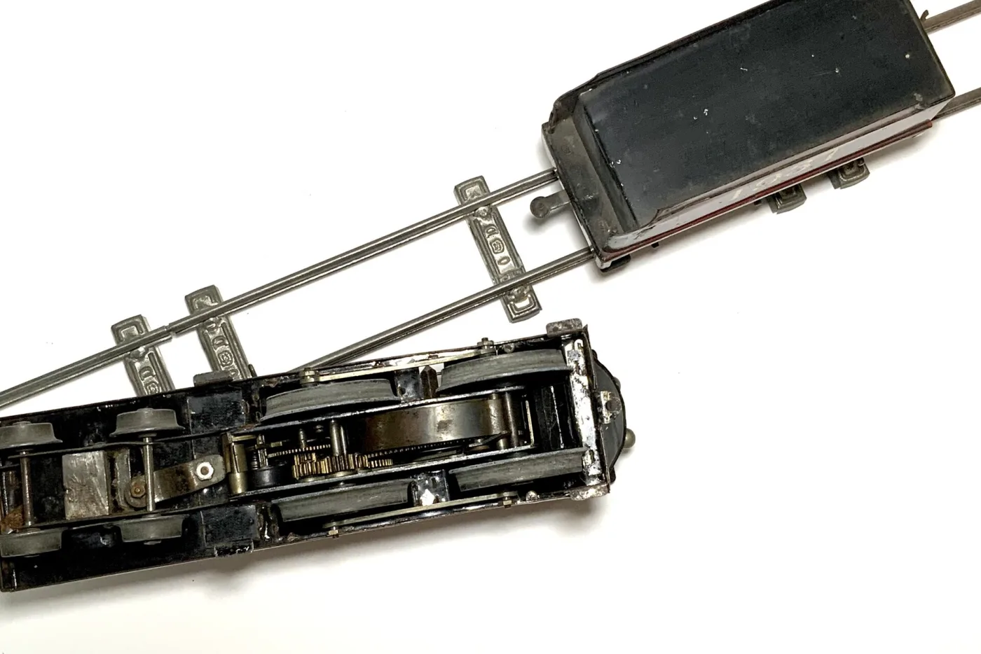 Underside of a tinplate toy locomotive showing an exposed clockwork gear train between the wheels