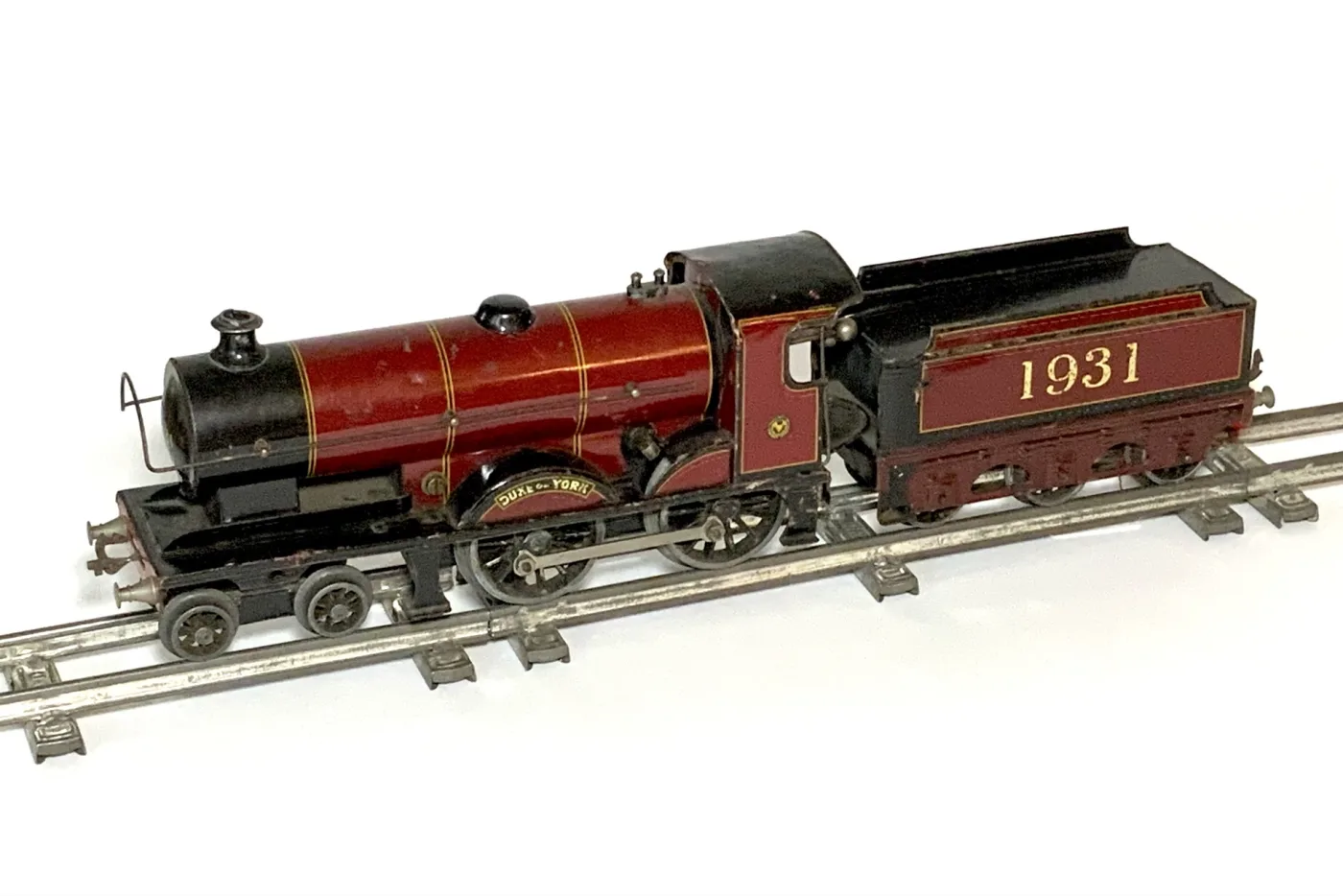 Crimson tinplate toy locomotive and tender lettered 1931, standing on two-rail tinplate track