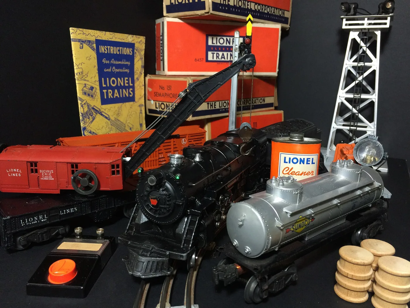 Toy locomotive, crane car and tank car in front of stacked orange catalogue boxes and an instruction booklet