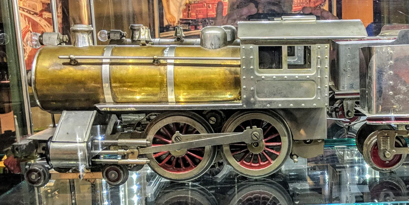 Early toy locomotive with a polished brass boiler, riveted nickel cab and red-spoked driving wheels
