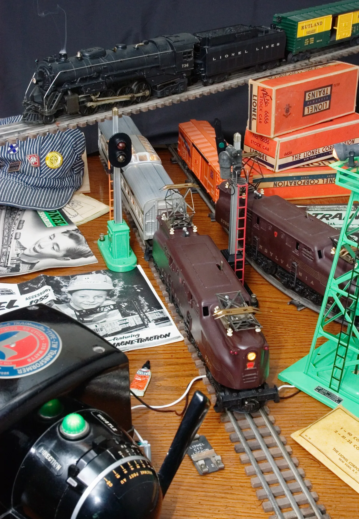 Postwar toy trains, orange catalogue boxes, a transformer and a leaflet spread across a table