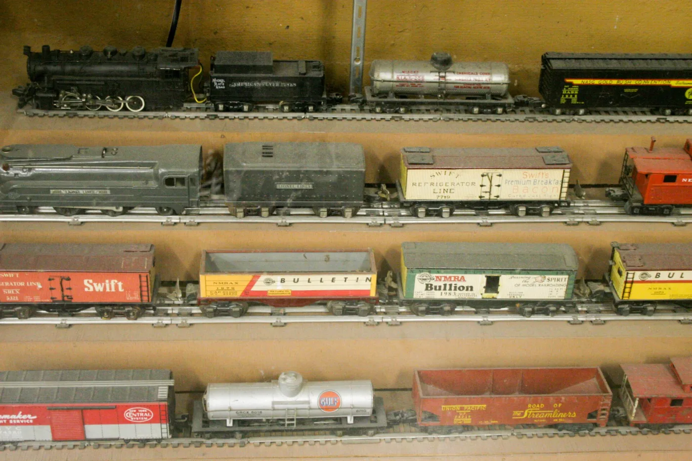 Four shelves of American toy trains, the top shelf on two-rail track and the three below on three-rail track
