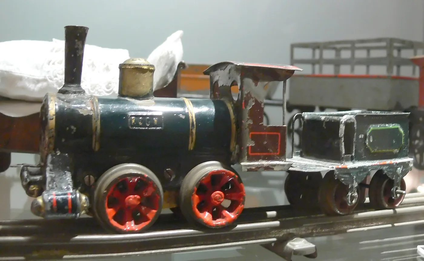 Dark green hand-painted tinplate locomotive with red spoked wheels and paint chipped to bare metal