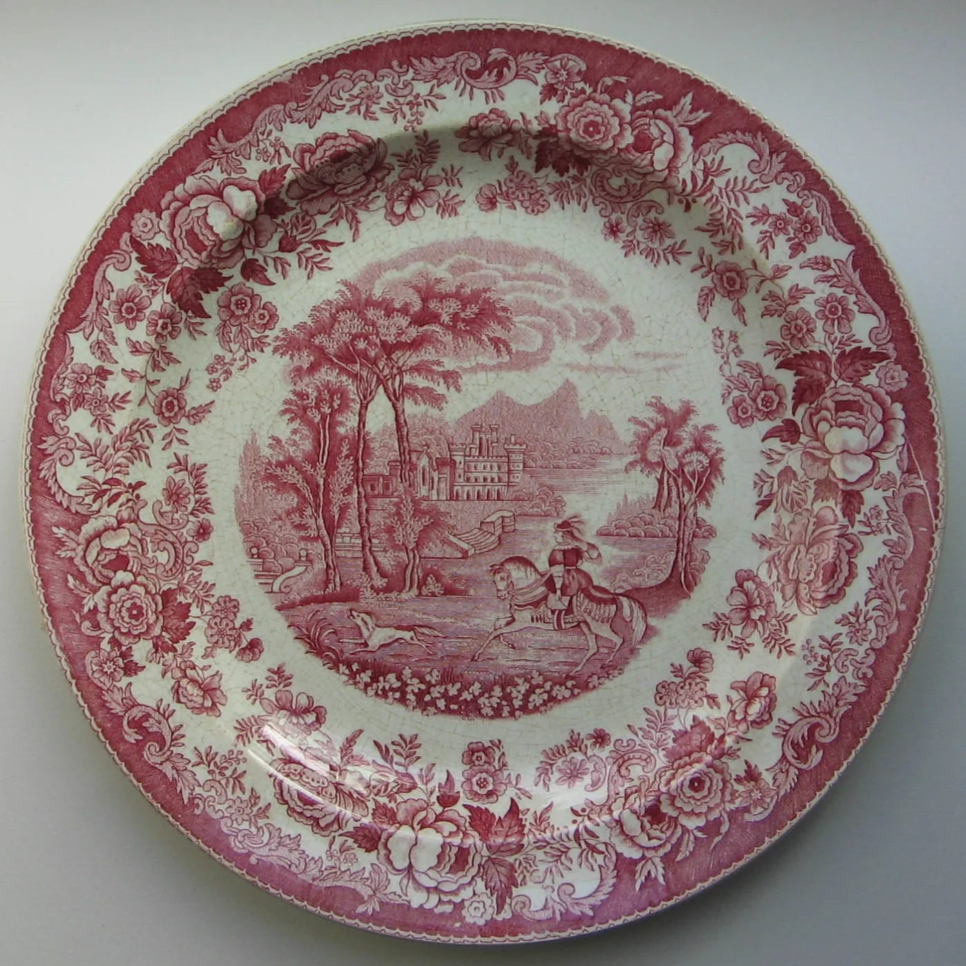 Plate transfer printed in red with a central scene of a figure by a lake before a domed building, inside a dense border of flowers and scrollwork