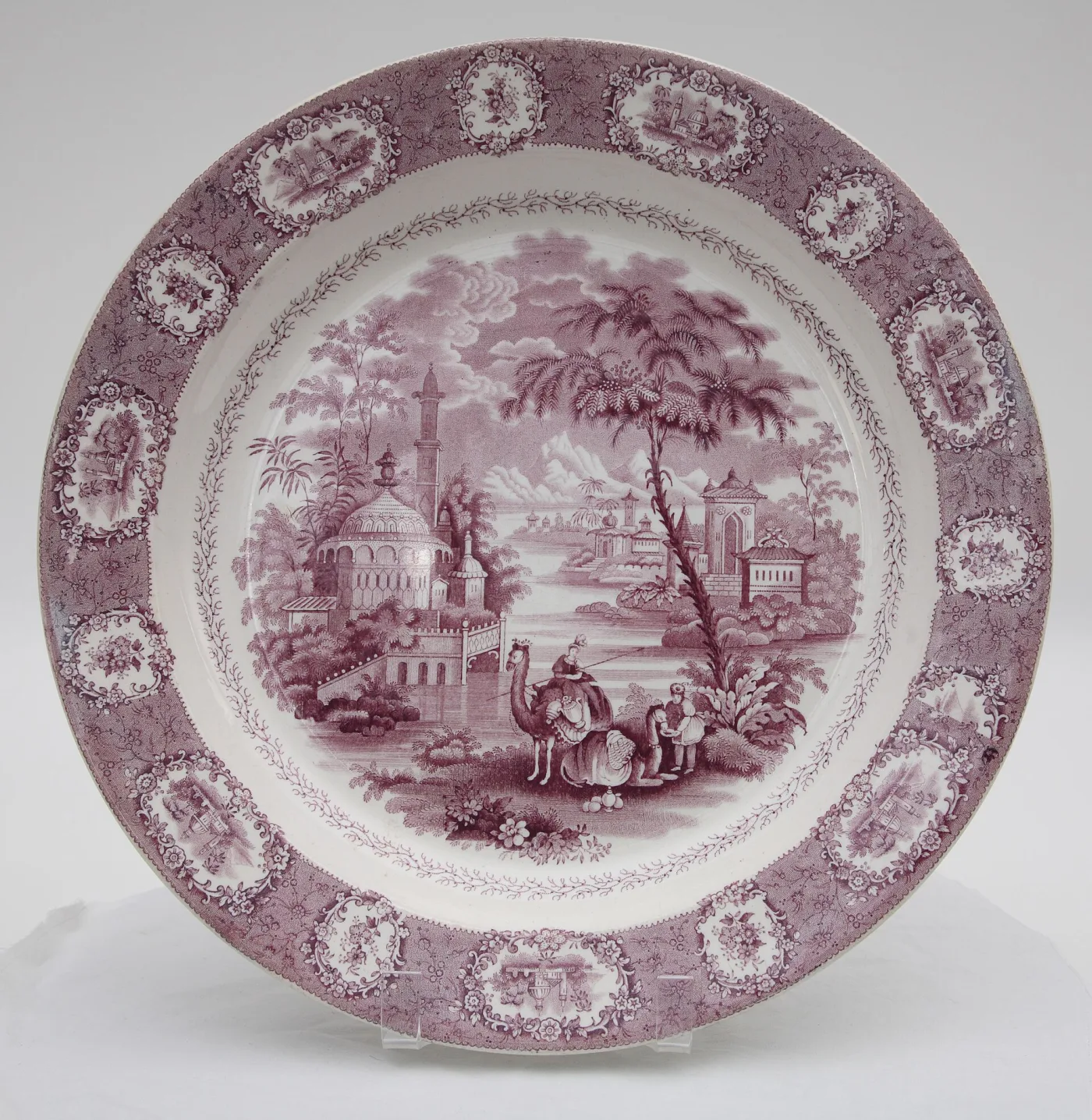 Deep circular platter printed in violet with oval vignettes of a domed building on the rim and a wider scene in the well, on a stippled ground of trailing branches and small flowers