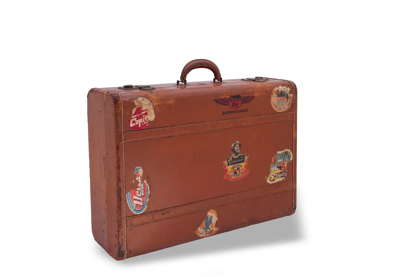 Tan leather suitcase with rounded corners and a leather handle, its lid covered in several coloured paper travel labels from hotels and shipping lines