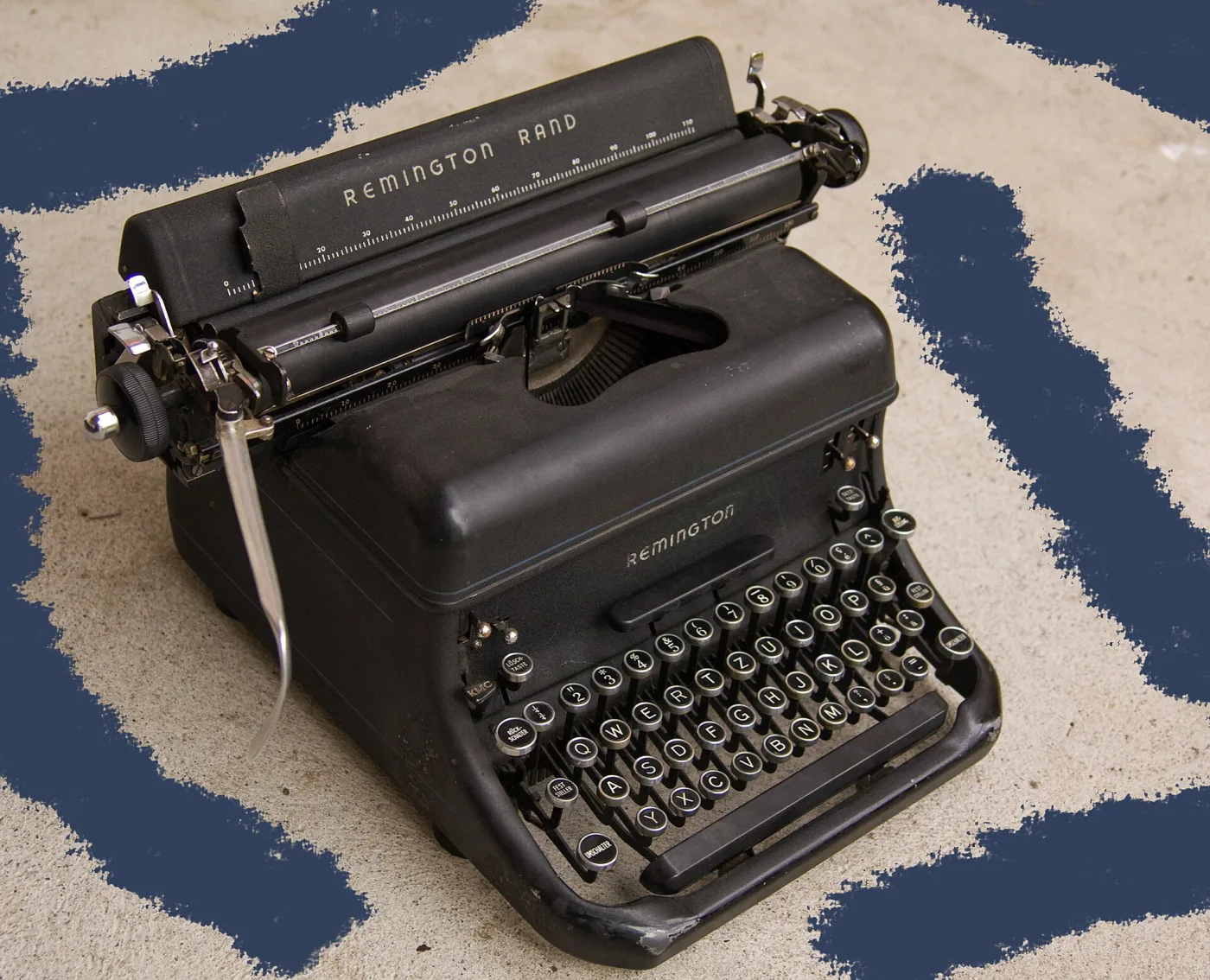 Heavy black desktop typewriter of the late 1940s with an enclosed body, a rounded frame, glass-topped round keys and a wide carriage, standing on a patterned rug