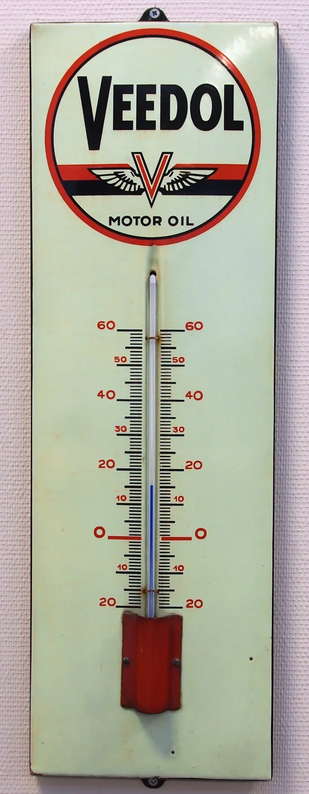 Tall narrow enamel advertising thermometer for Veedol motor oil, white with a red and black brand shield at the top, a red-filled glass tube down the centre and a numbered scale either side