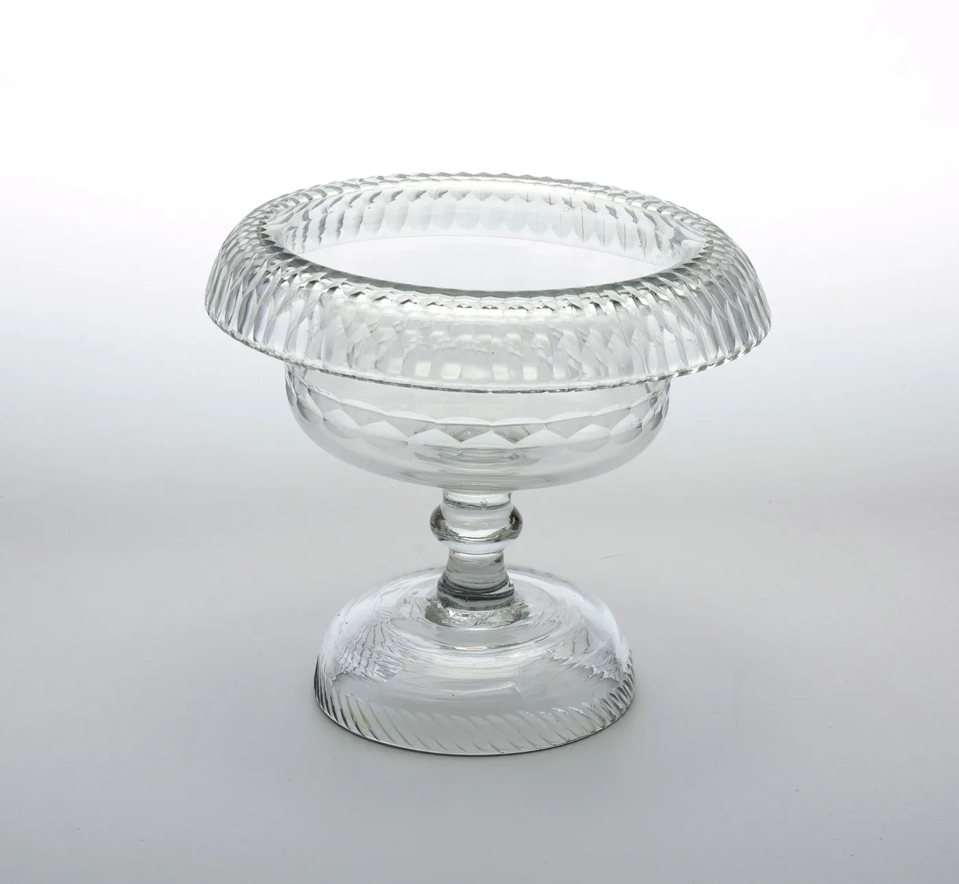 Clear glass footed bowl of about 1800 with a wide turned-over rim cut in bands of facets, a knopped stem and a domed foot
