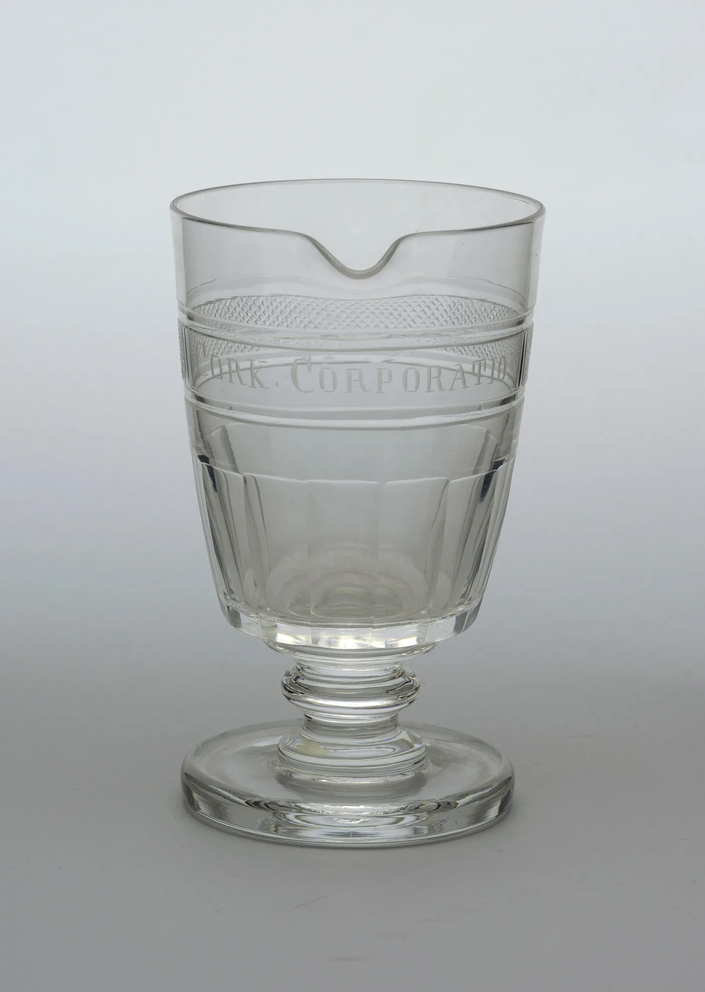 Footed mixing glass with a pouring lip, cut vertical flutes and an engraved band reading Cork Corporation between hatched borders
