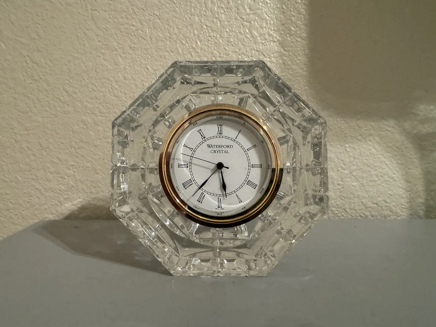 Octagonal cut-crystal desk clock with a gilt bezel and a white dial reading Waterford Crystal in Roman numerals
