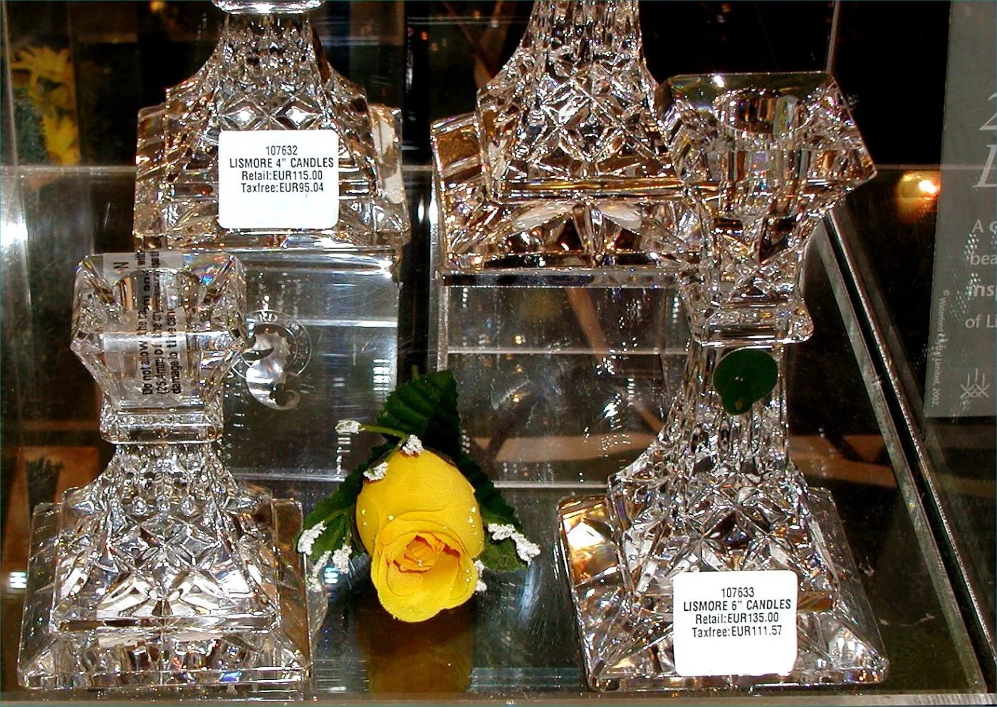 Shop display case holding four cut-crystal candlesticks in two sizes, with printed price tickets reading Lismore 4 inch candles and Lismore 6 inch candles