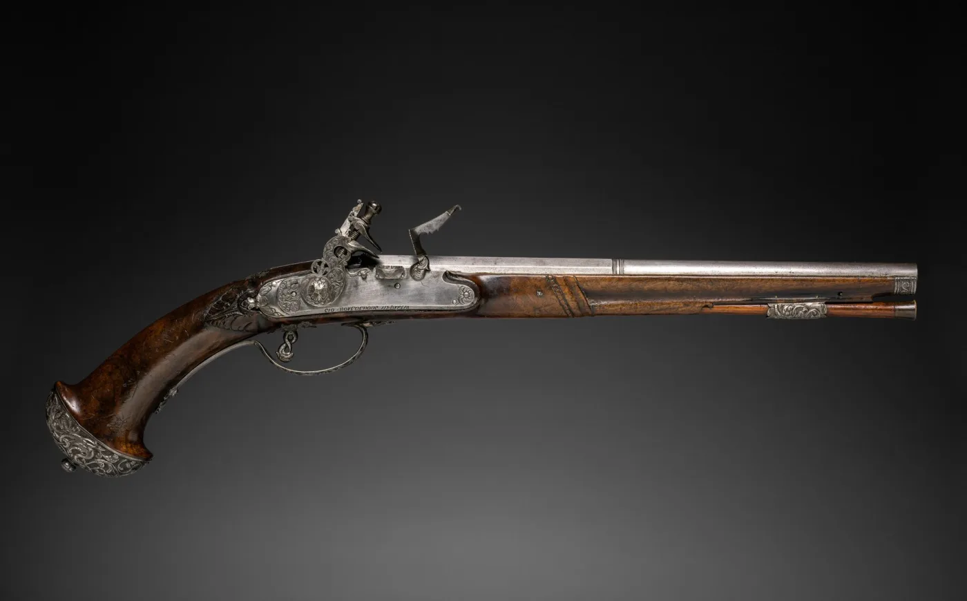 Late seventeenth-century flintlock pistol on a black ground, with a long tapering barrel, a scrolled steel lock plate, a carved walnut stock and a shaped steel butt