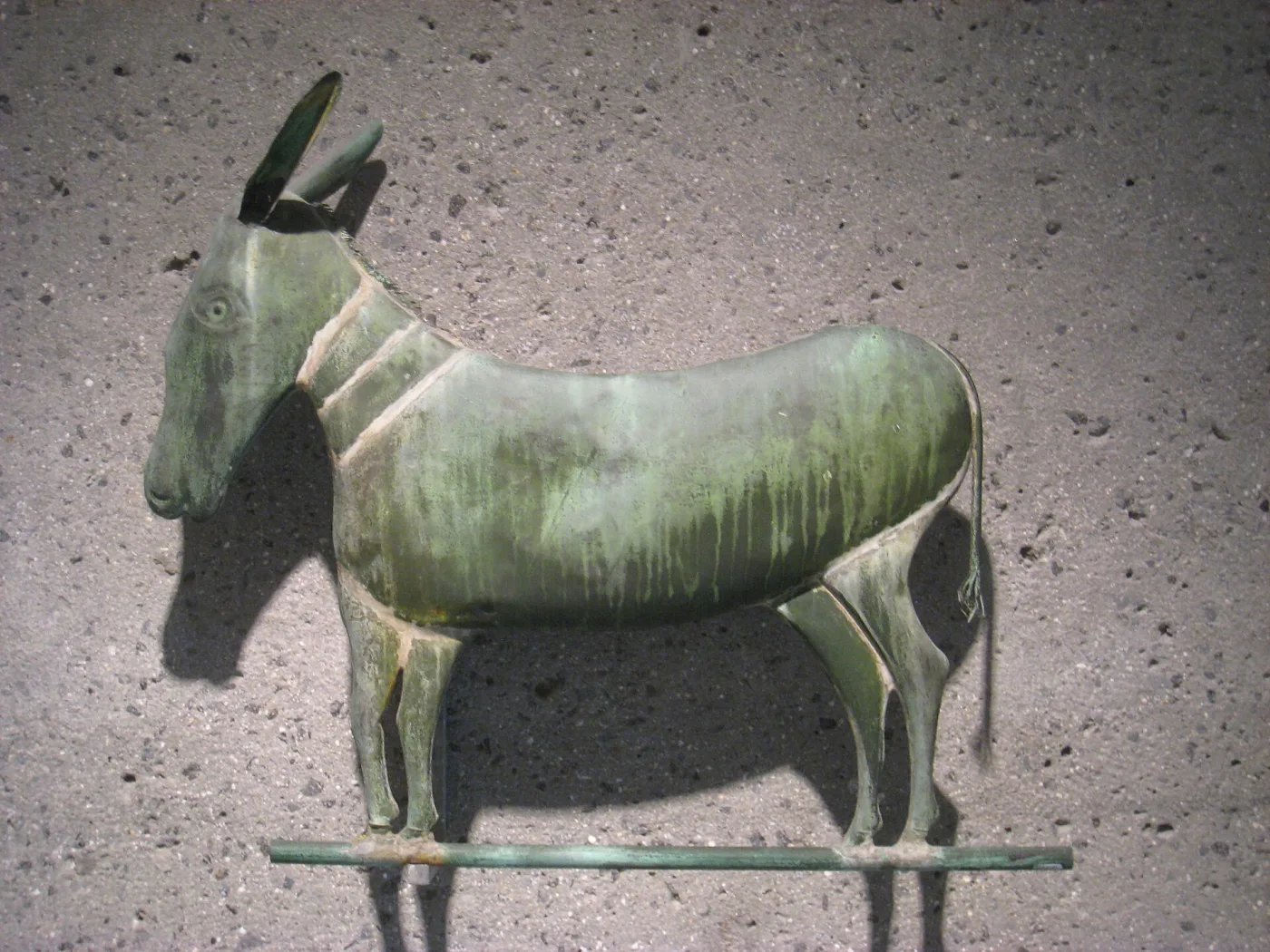 A weathervane in the form of a donkey, displayed against a plain wall in a museum gallery