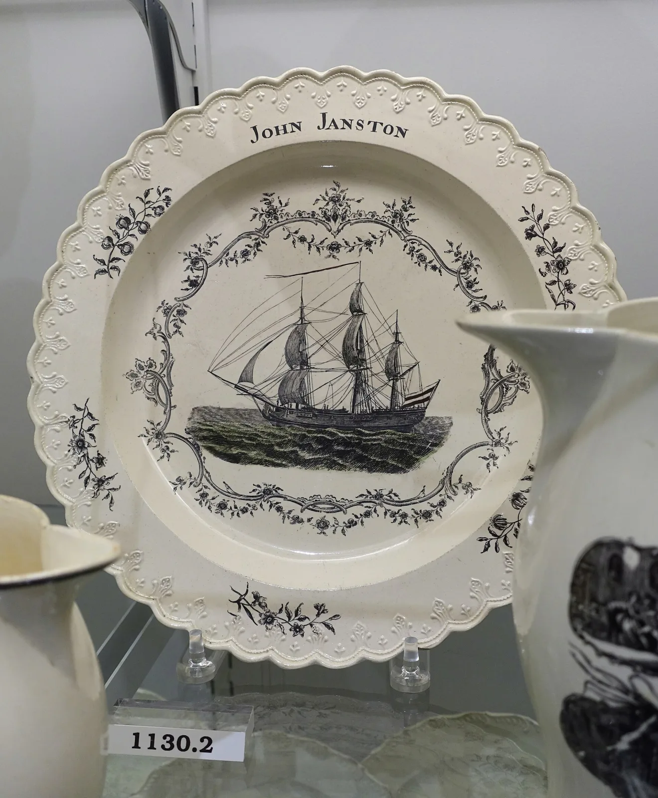 Creamware dish transfer-printed in black with a three-masted ship in full sail, encircled by a delicate floral wreath and the name JOHN JANSTON in capitals across the top