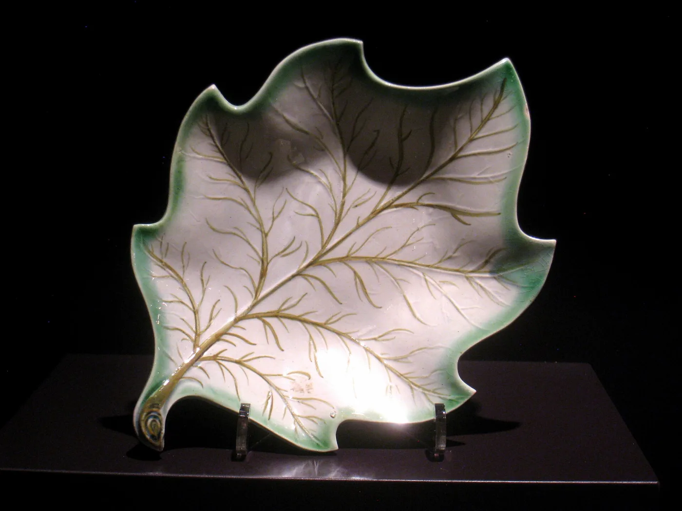 Shallow sweetmeat dish moulded as an overlapping leaf, its veins raised and its edges shaded green and brown against a pale ground