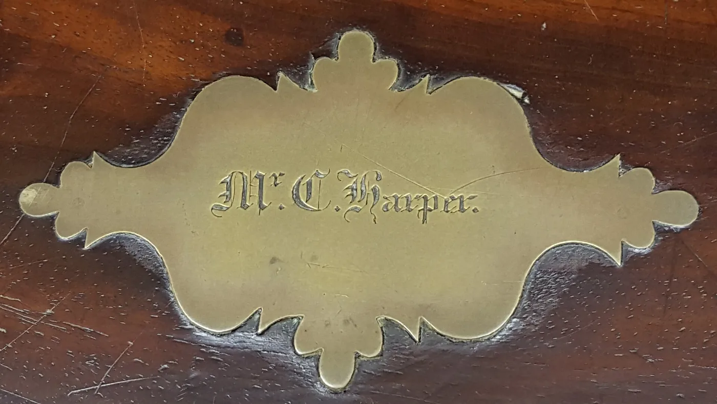 Shaped brass name plate with a scalloped rococo outline, screwed into dark polished wood and engraved in script with an owner's name