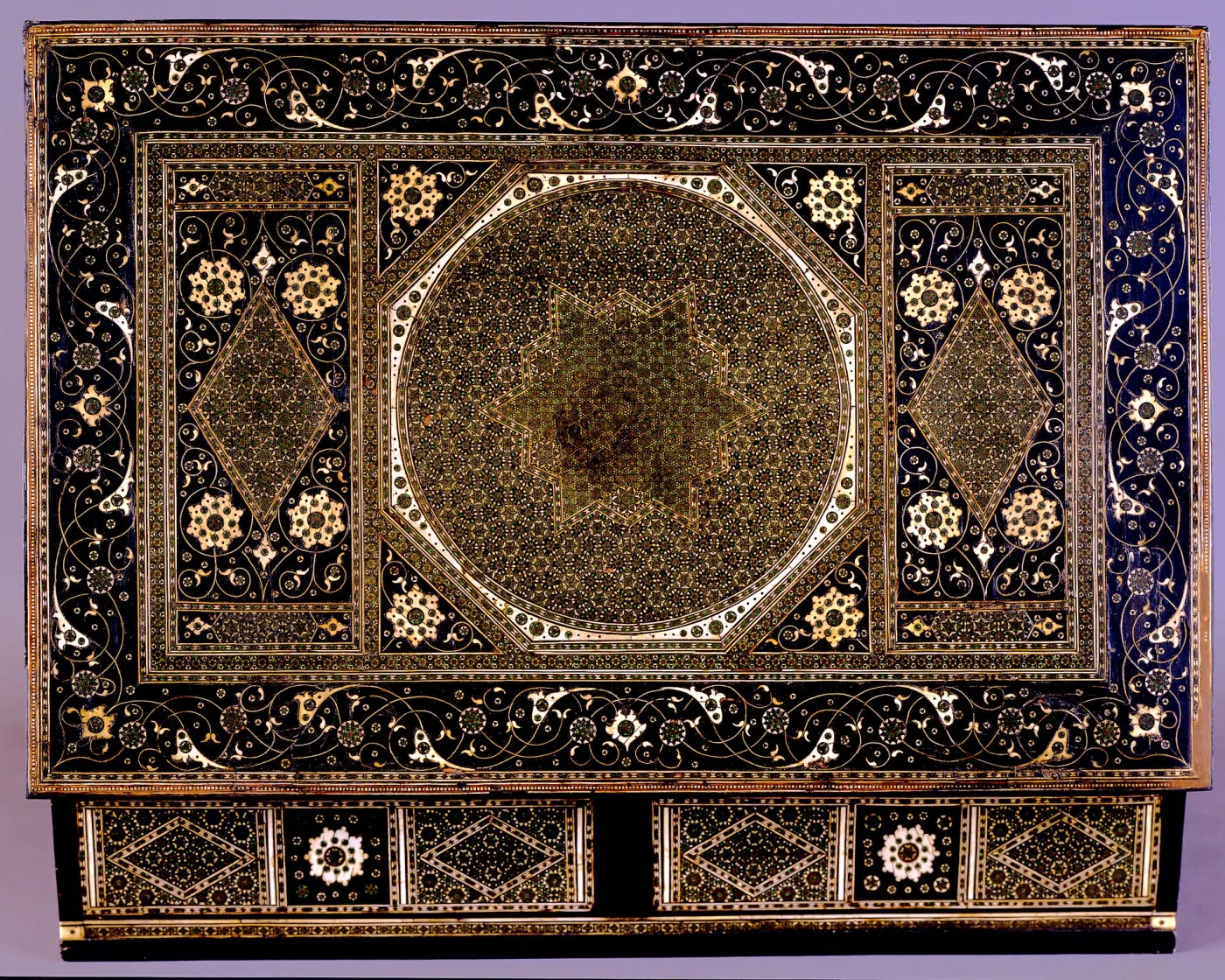 Close view of the lid of an inlaid writing box, its surface covered in a dense radiating star pattern of tiny bone, ebony and coloured wood tesserae inside multiple banded borders